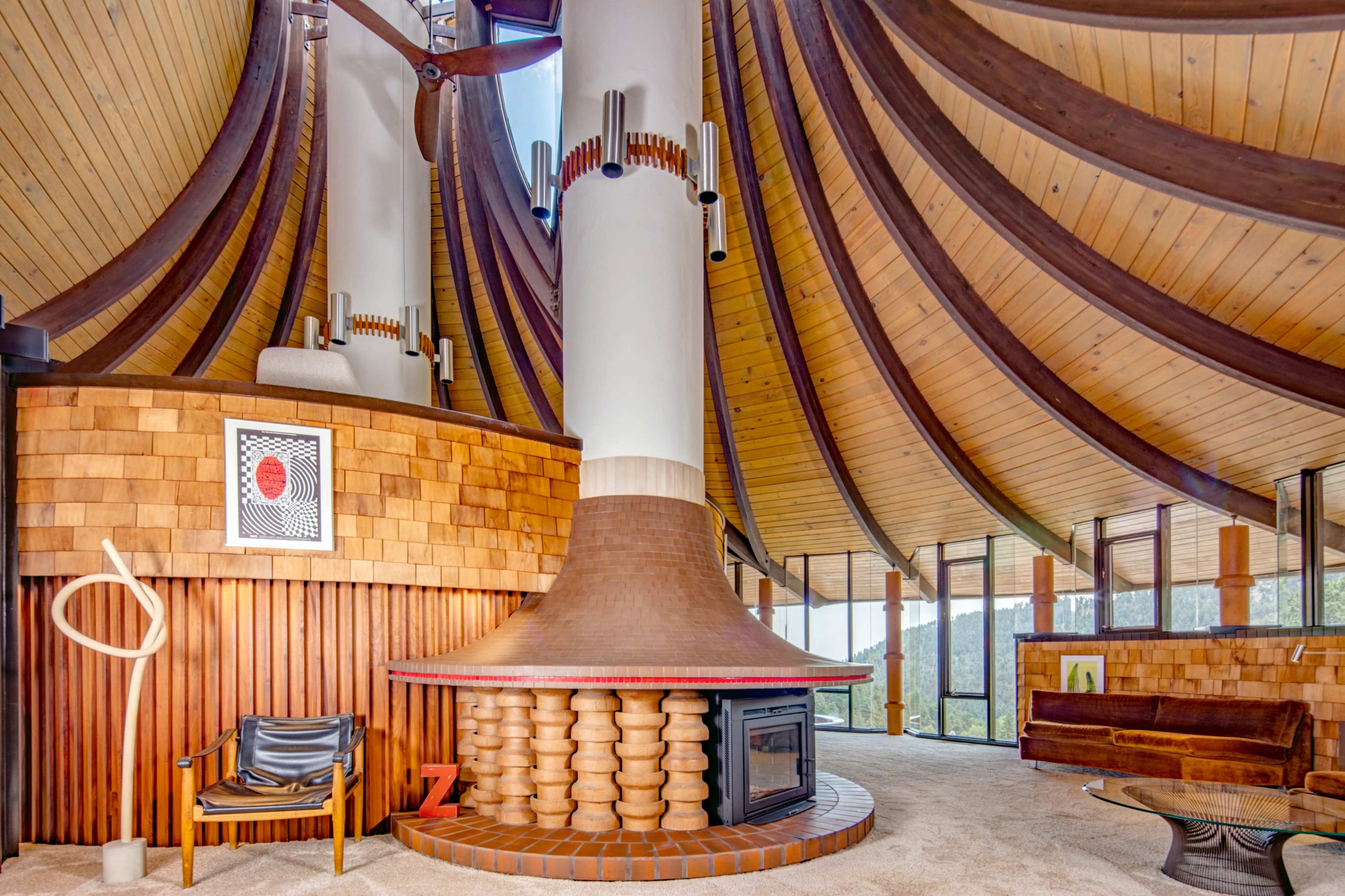 The interior of a uniquely designed architectural space features a prominent circular chimney surrounded by wooden accents and a combination of seating areas.
