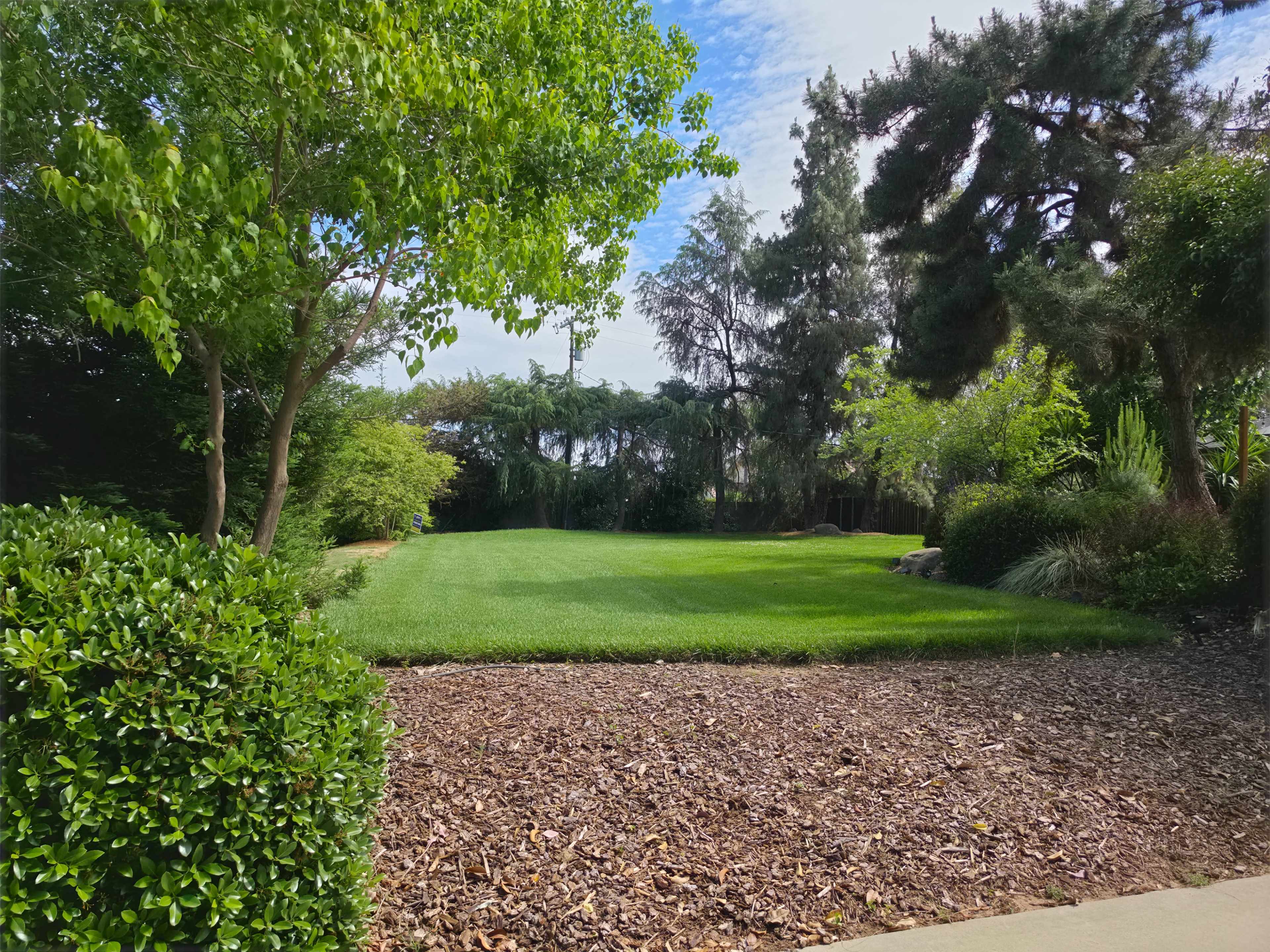 A green lawn bordered by shrubs and trees is visible under a partly cloudy sky.