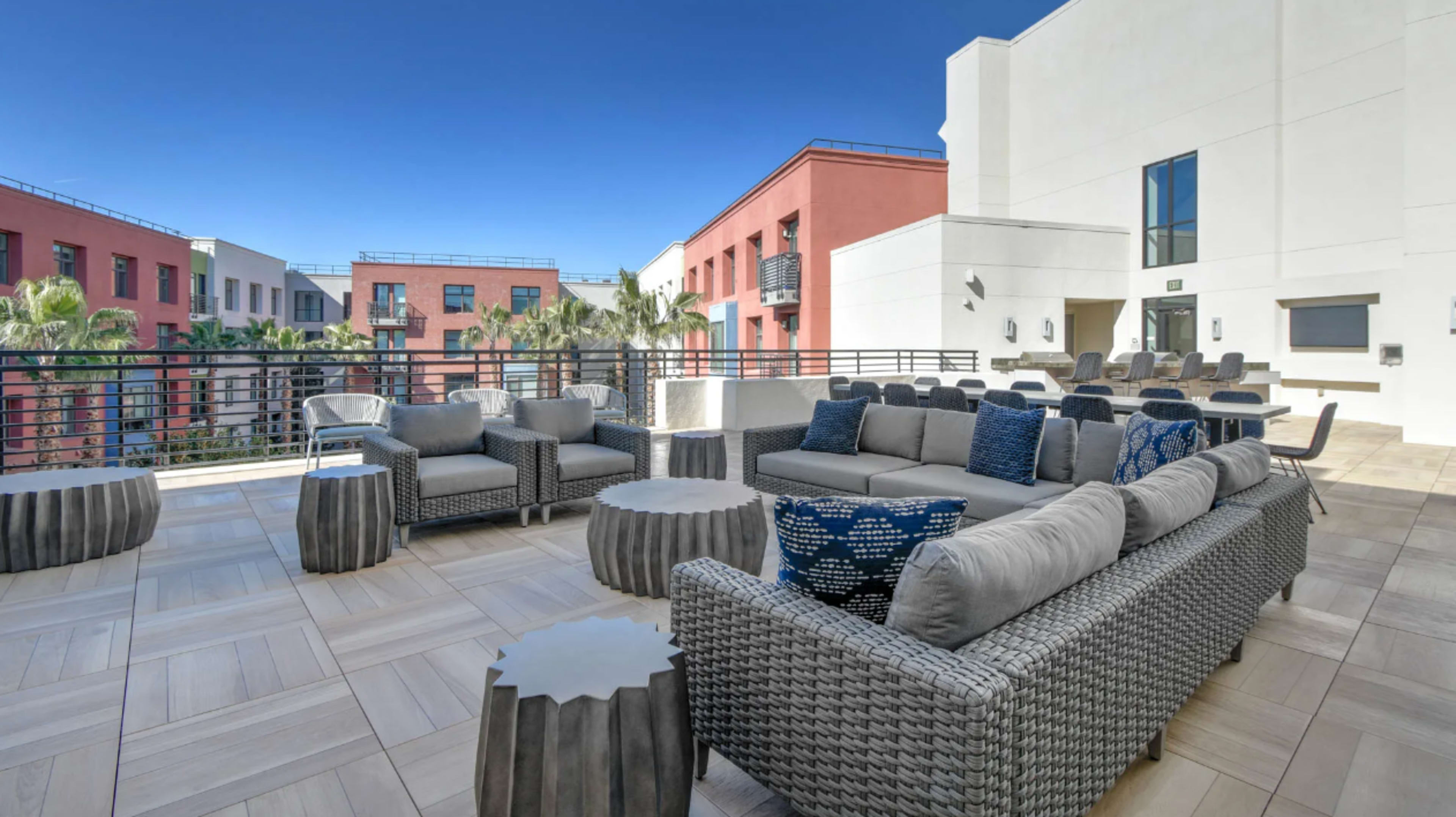 A modern outdoor lounge area featuring woven furniture, circular tables, and clear blue skies in the background.