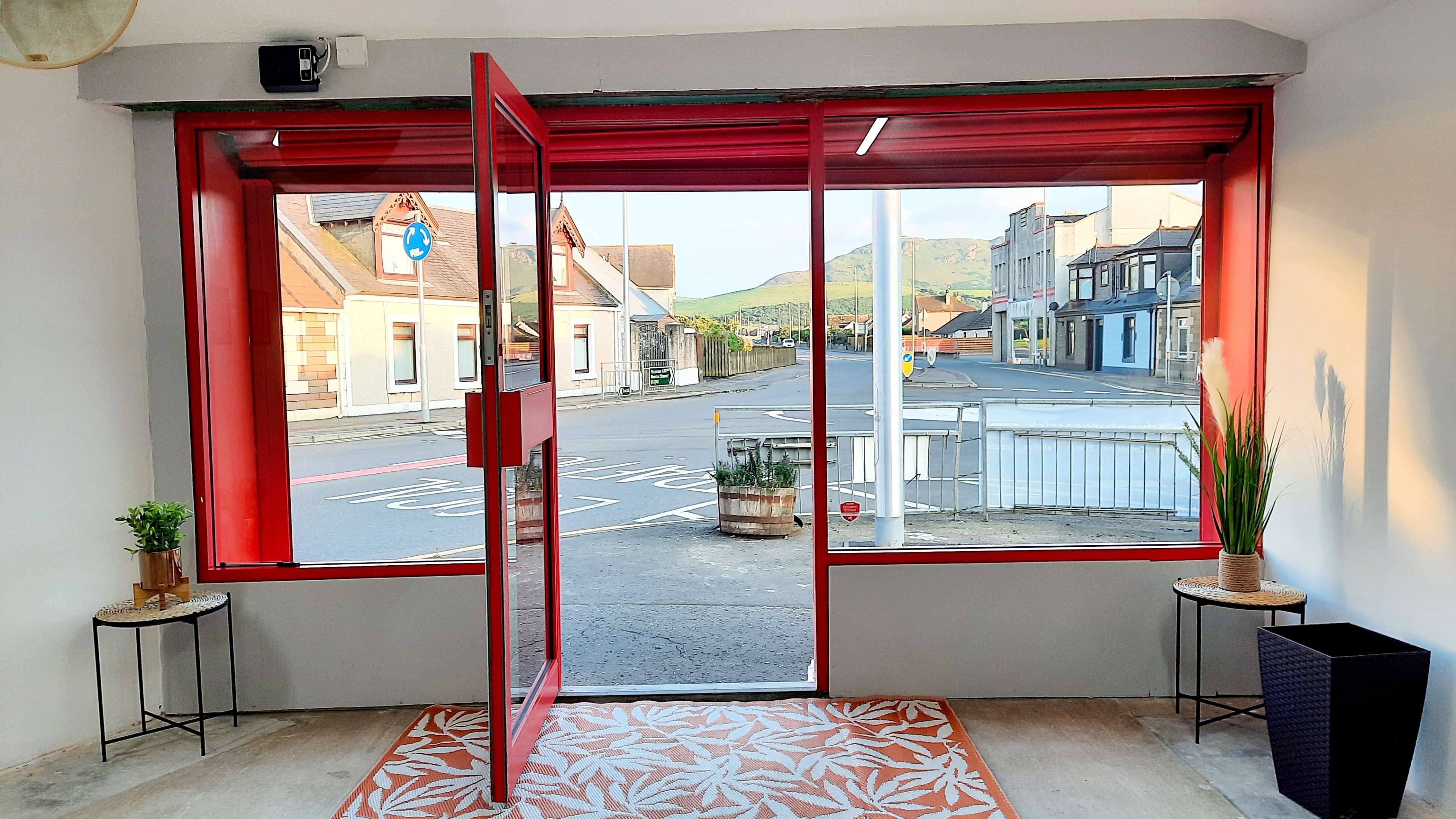 A red-framed doorway opens to a view of a street lined with buildings and mountains in the background.