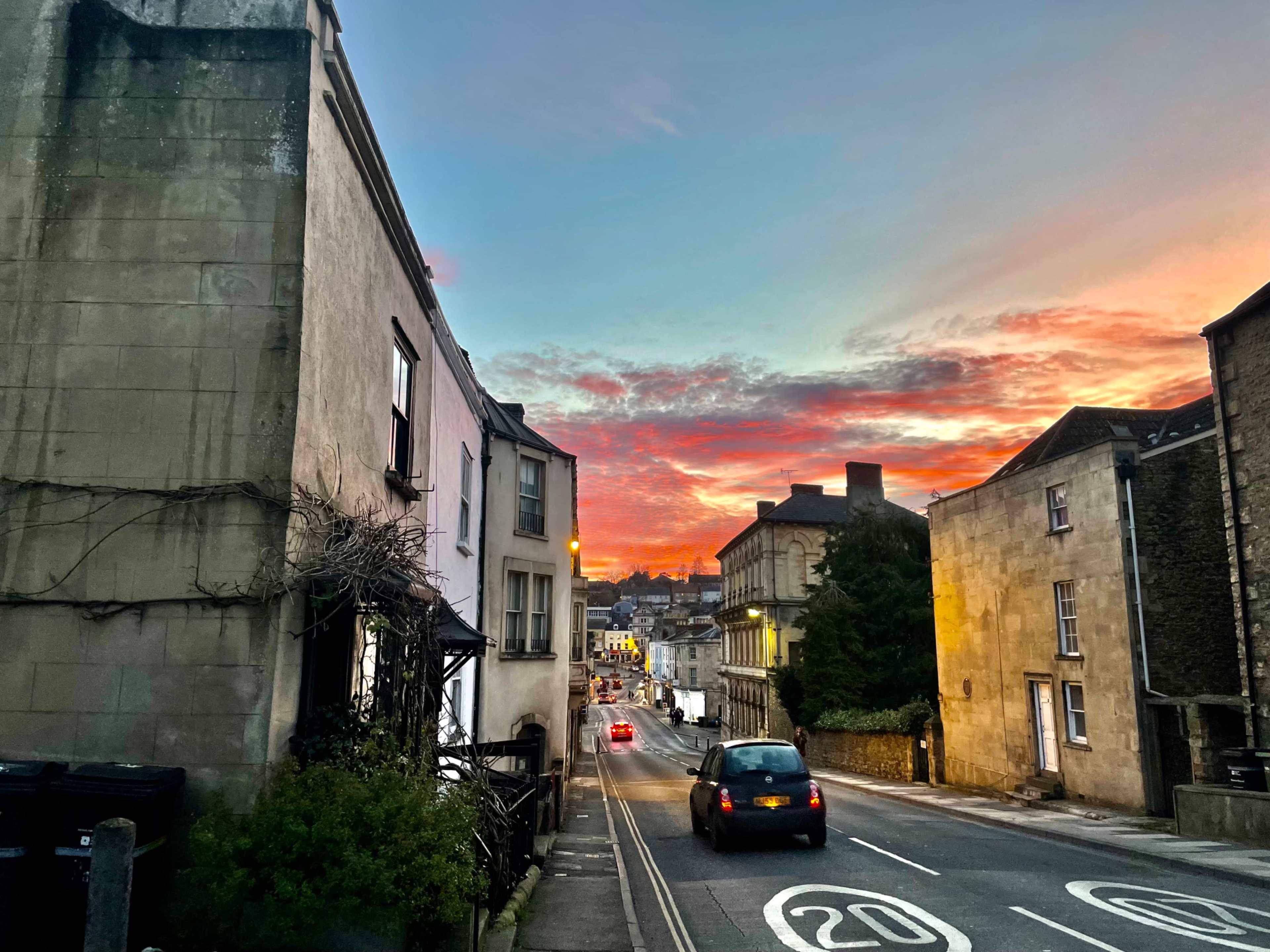 A narrow street lined with buildings on either side, illuminated by a colorful sunset in the background.