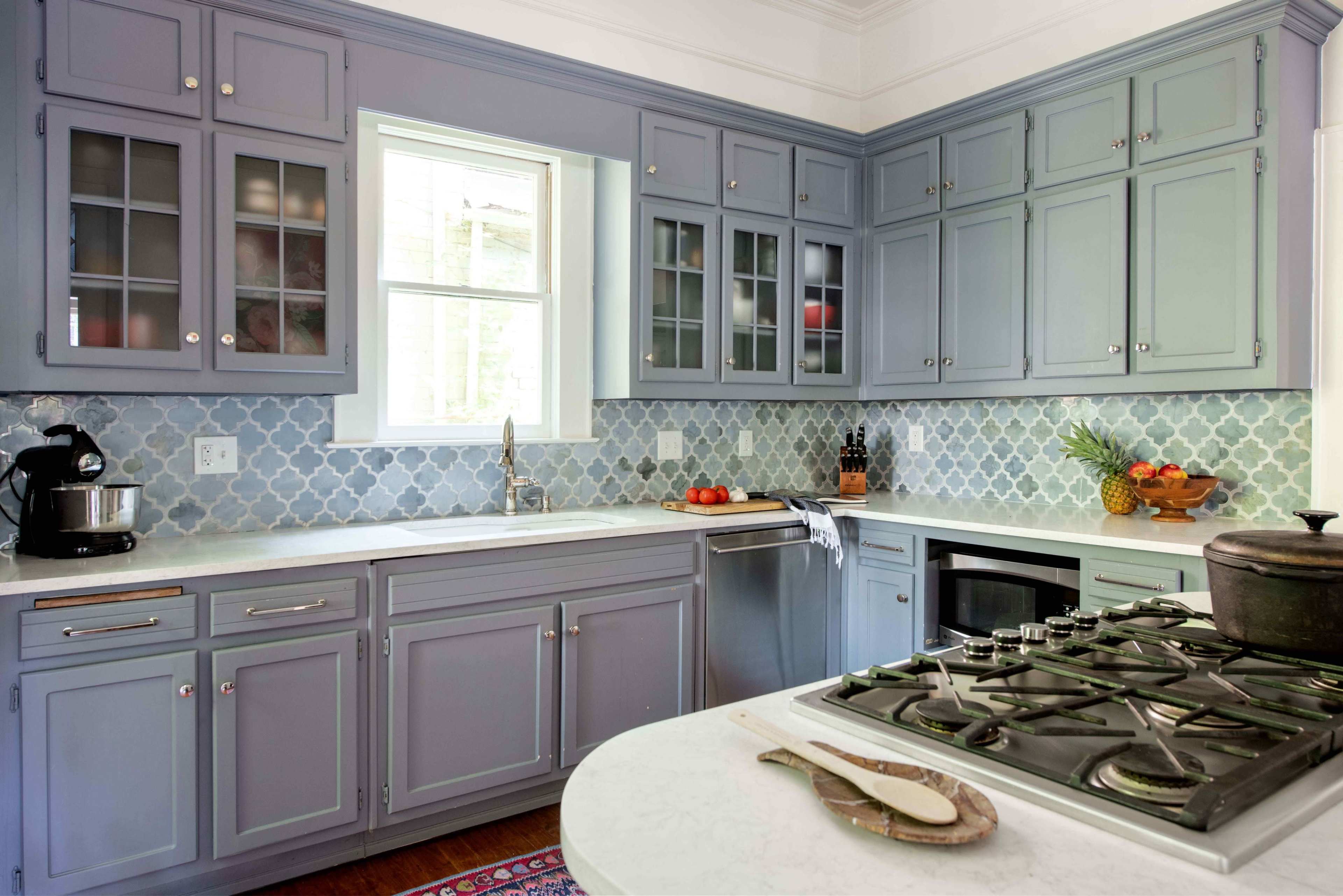 A modern kitchen features blue cabinets, a white counter, and a gas stove with a view of a window.