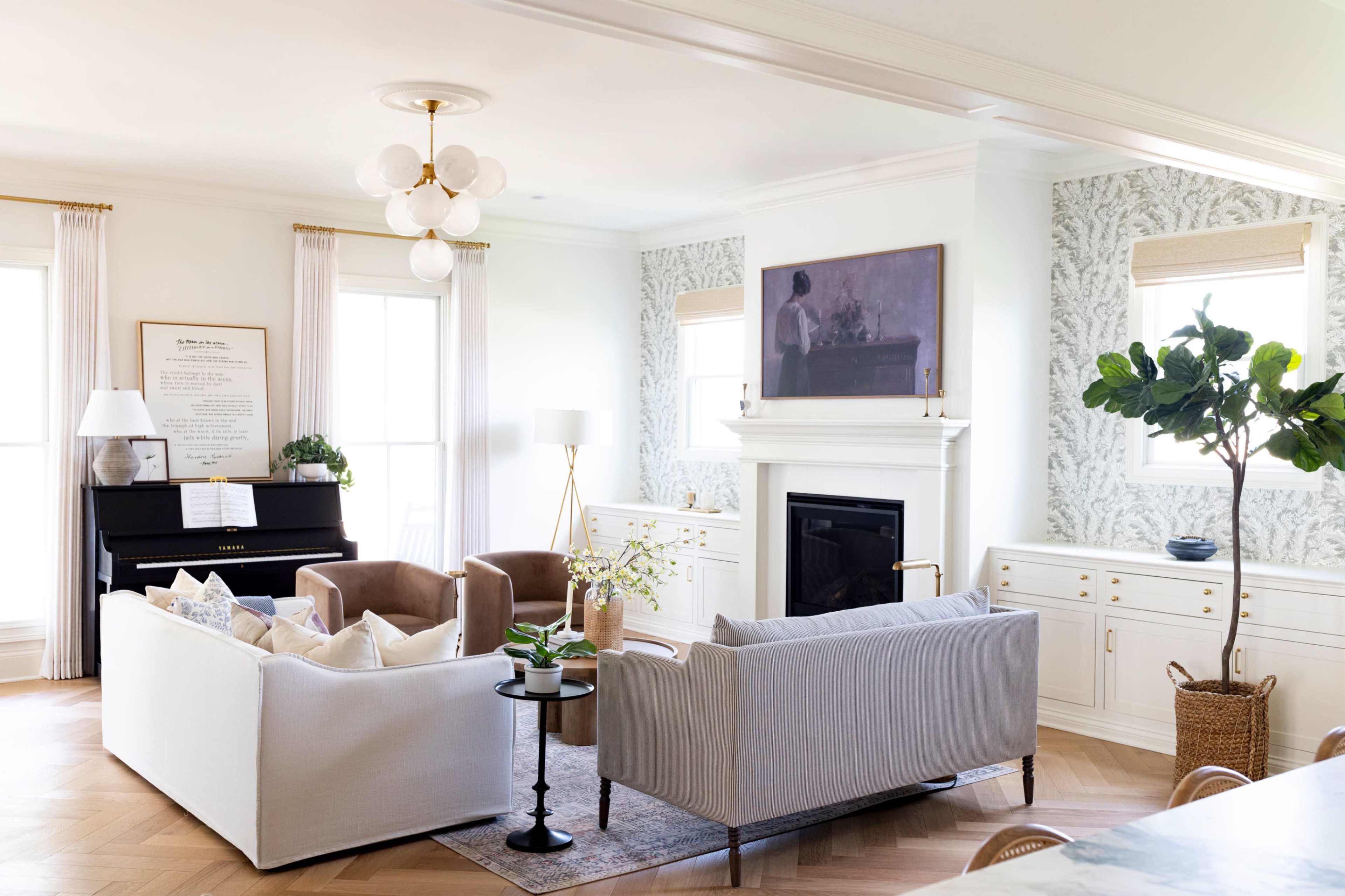 The image shows a modern living room featuring a piano, white cabinetry, a fireplace, and a mix of upholstered furniture arranged around a coffee table.