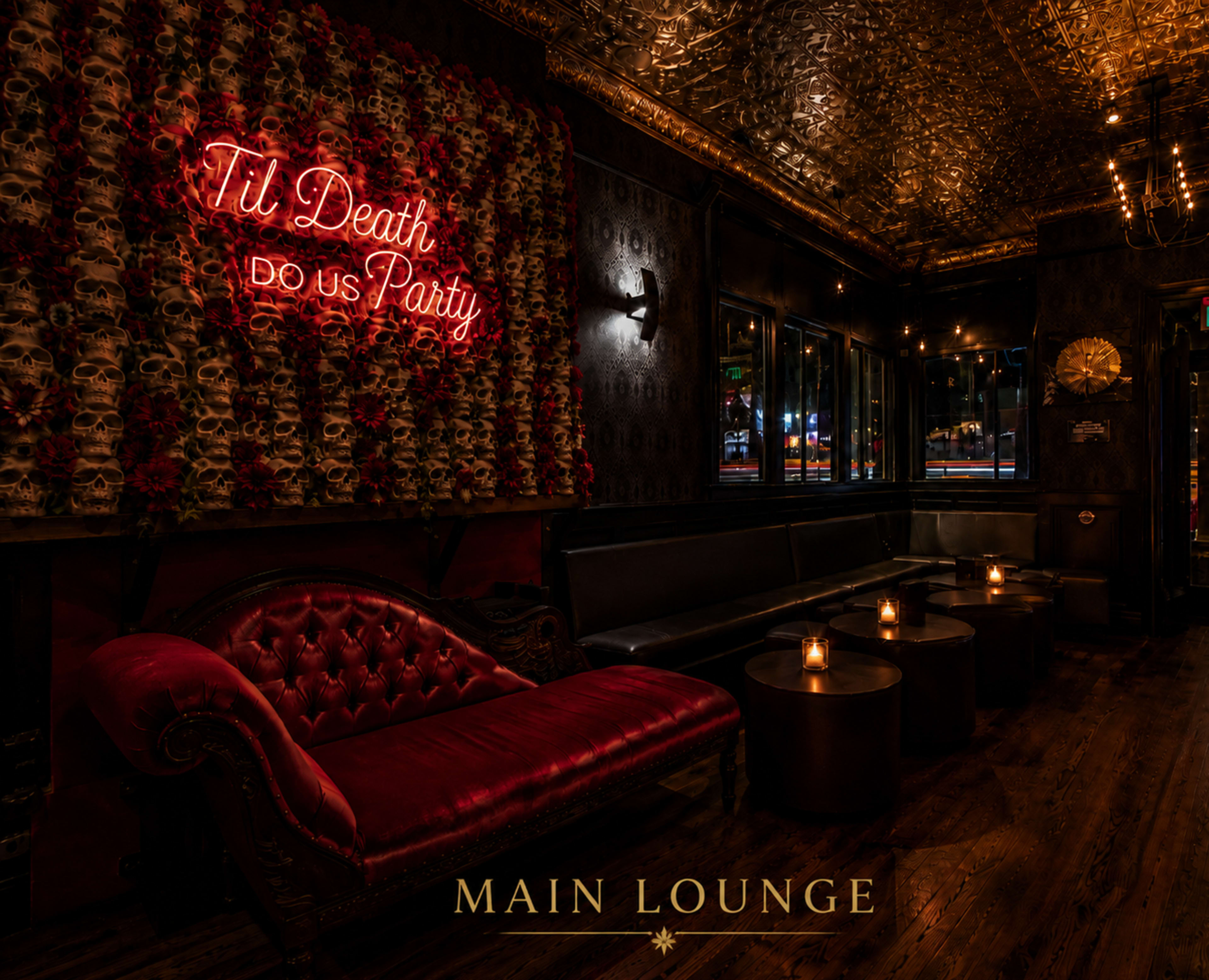 The image depicts a dimly lit lounge featuring a red velvet couch, a wall adorned with a floral design and a neon sign that reads "Til Death Do Us Party," along with candlelit tables.