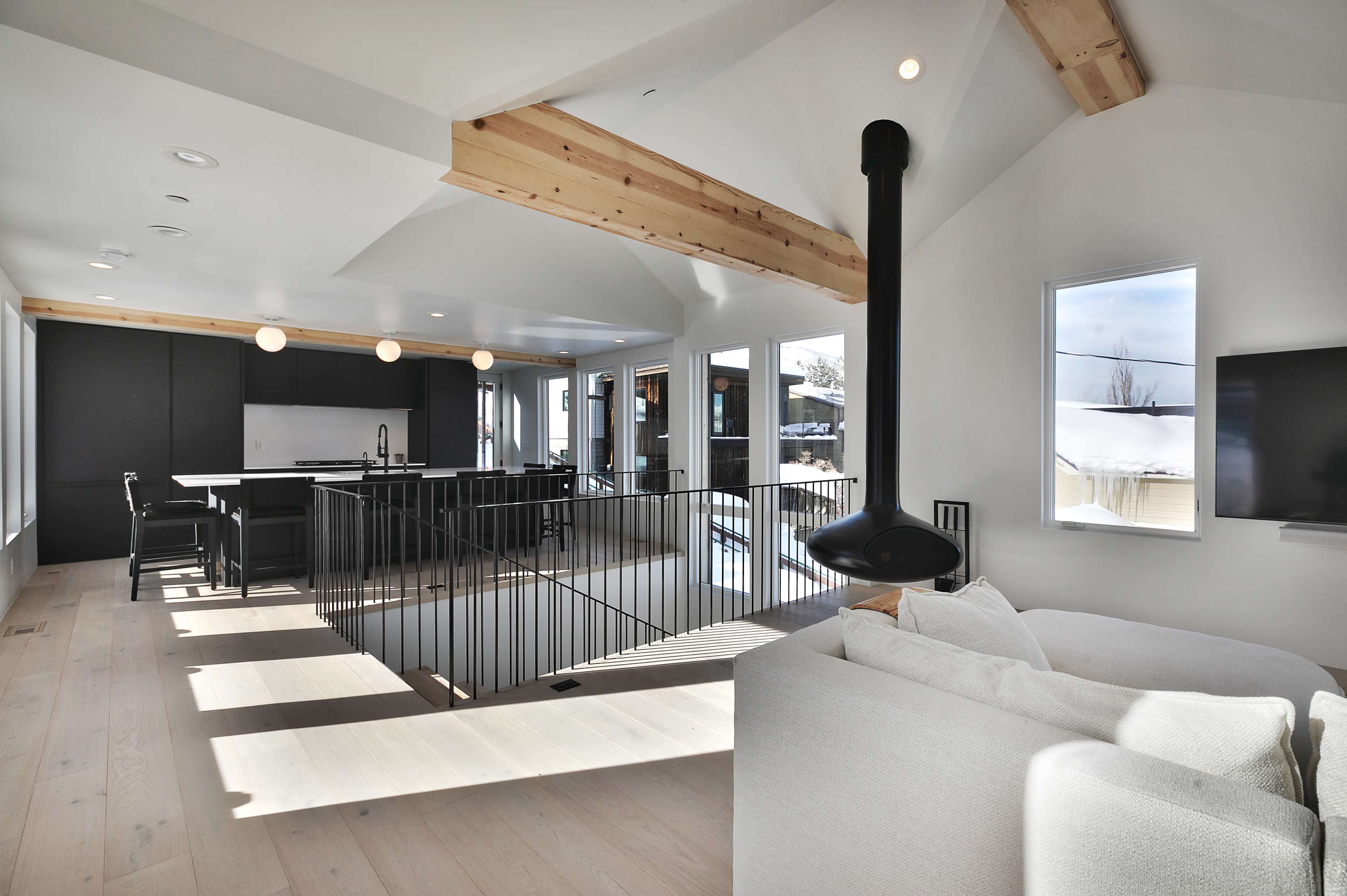 A modern interior space with high ceilings, large windows, and a kitchen area visible in the background.