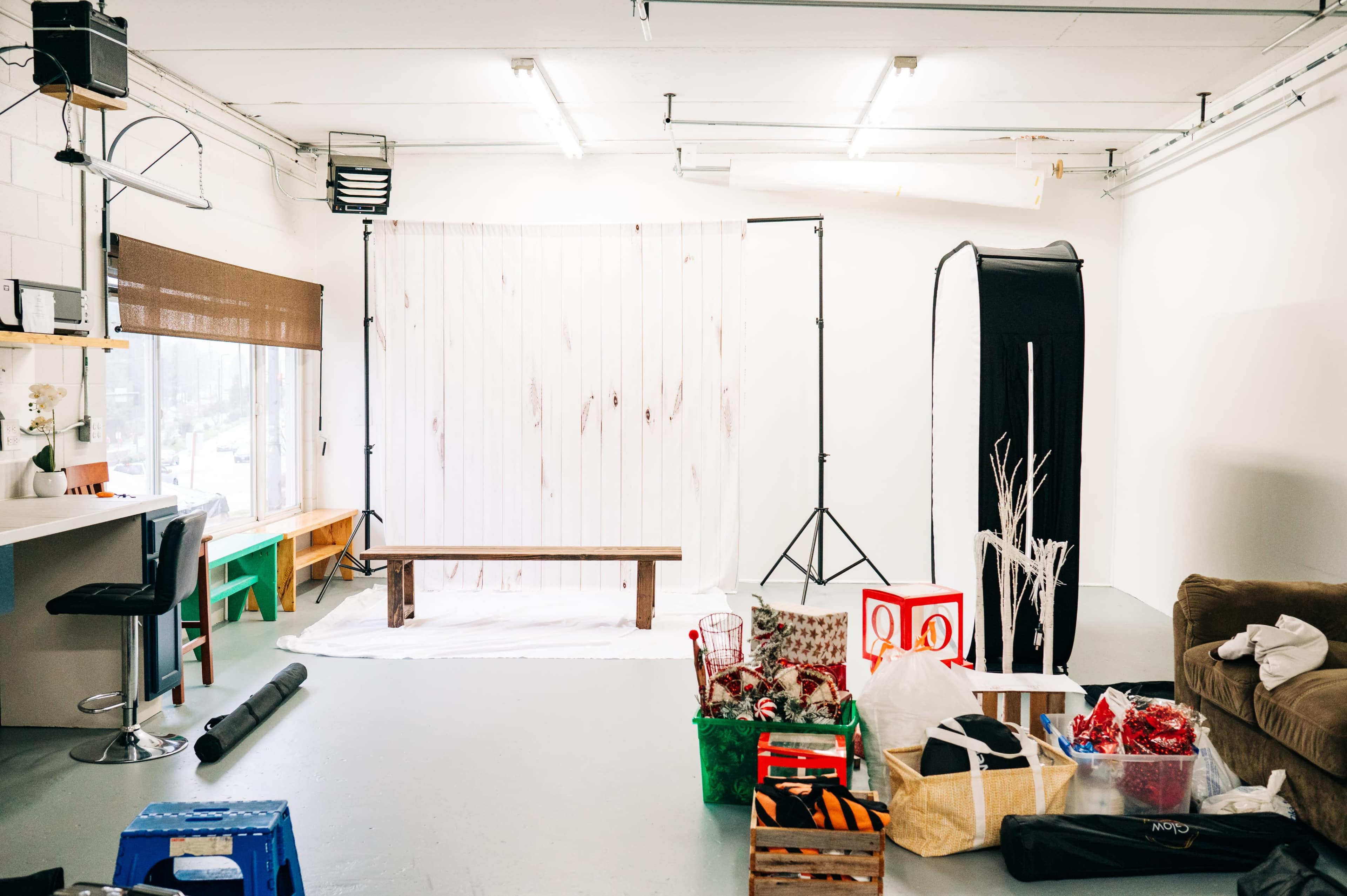 A photography studio is set up with a wooden bench, backdrop supports, and various props scattered across the floor.