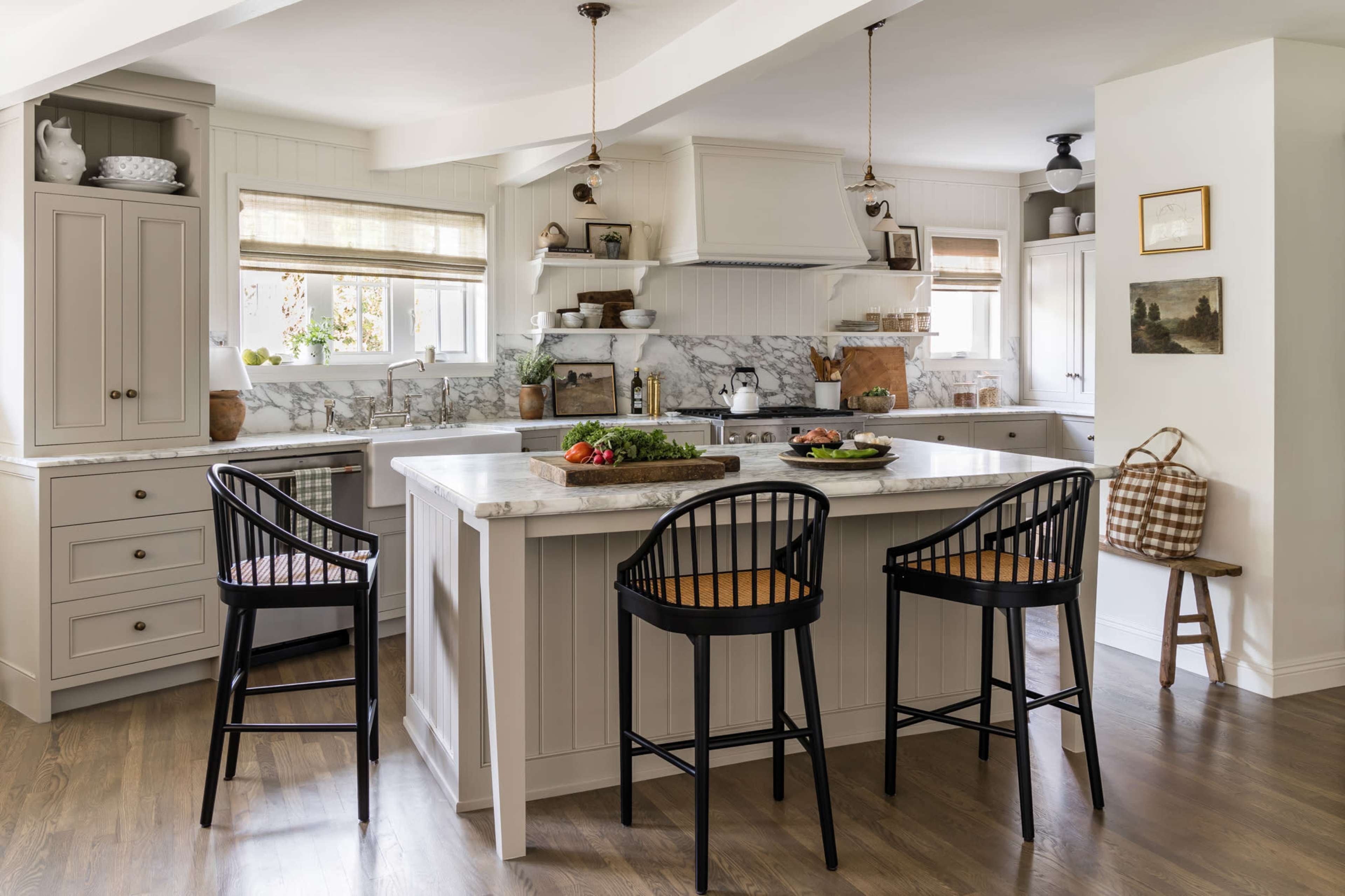 A modern kitchen with white cabinetry, a marble countertop, and black bar stools positioned around a large island.