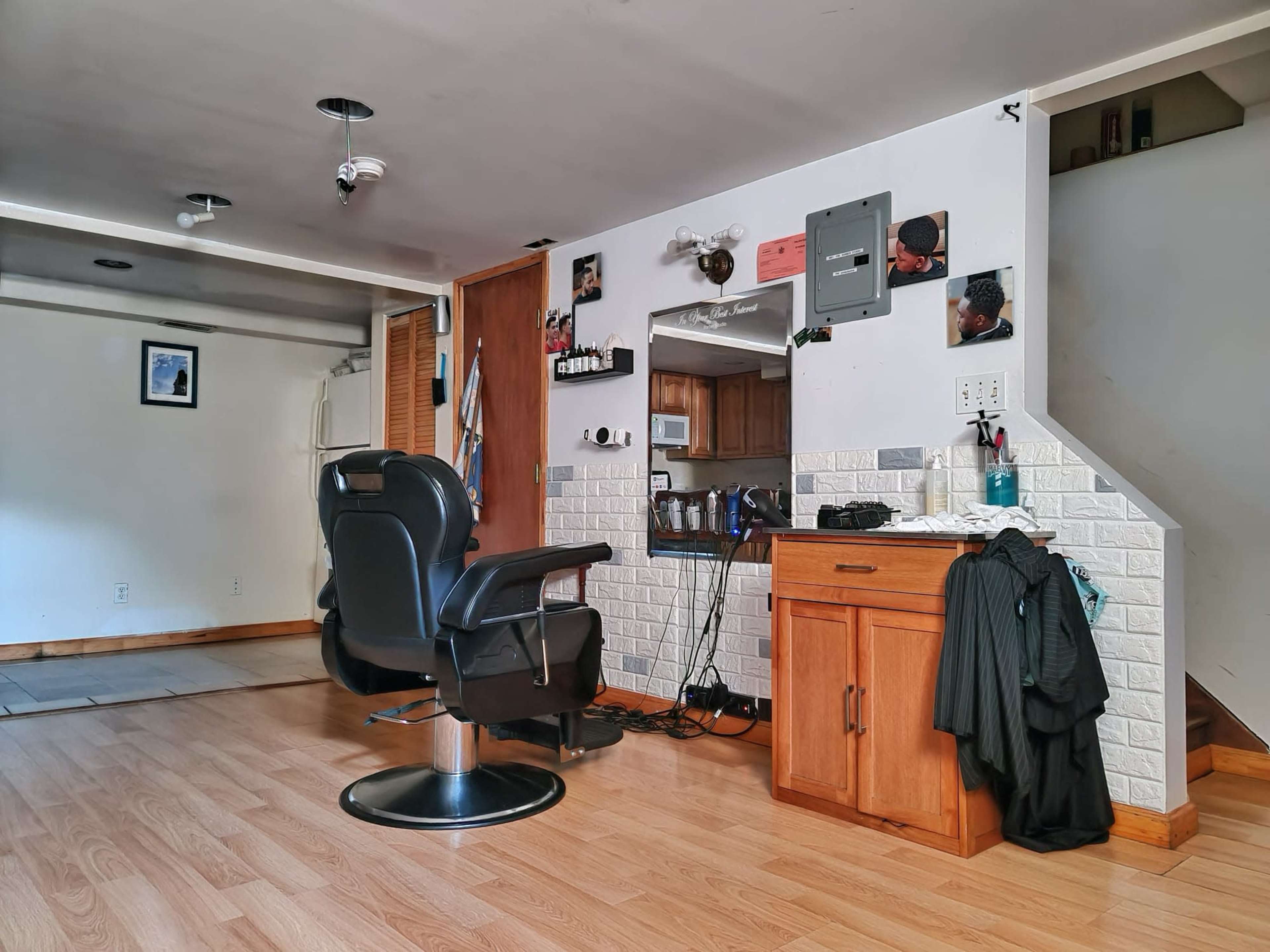 The image shows a corner of a hair salon featuring a black barber chair, a wooden vanity with hair products, and various wall decorations.