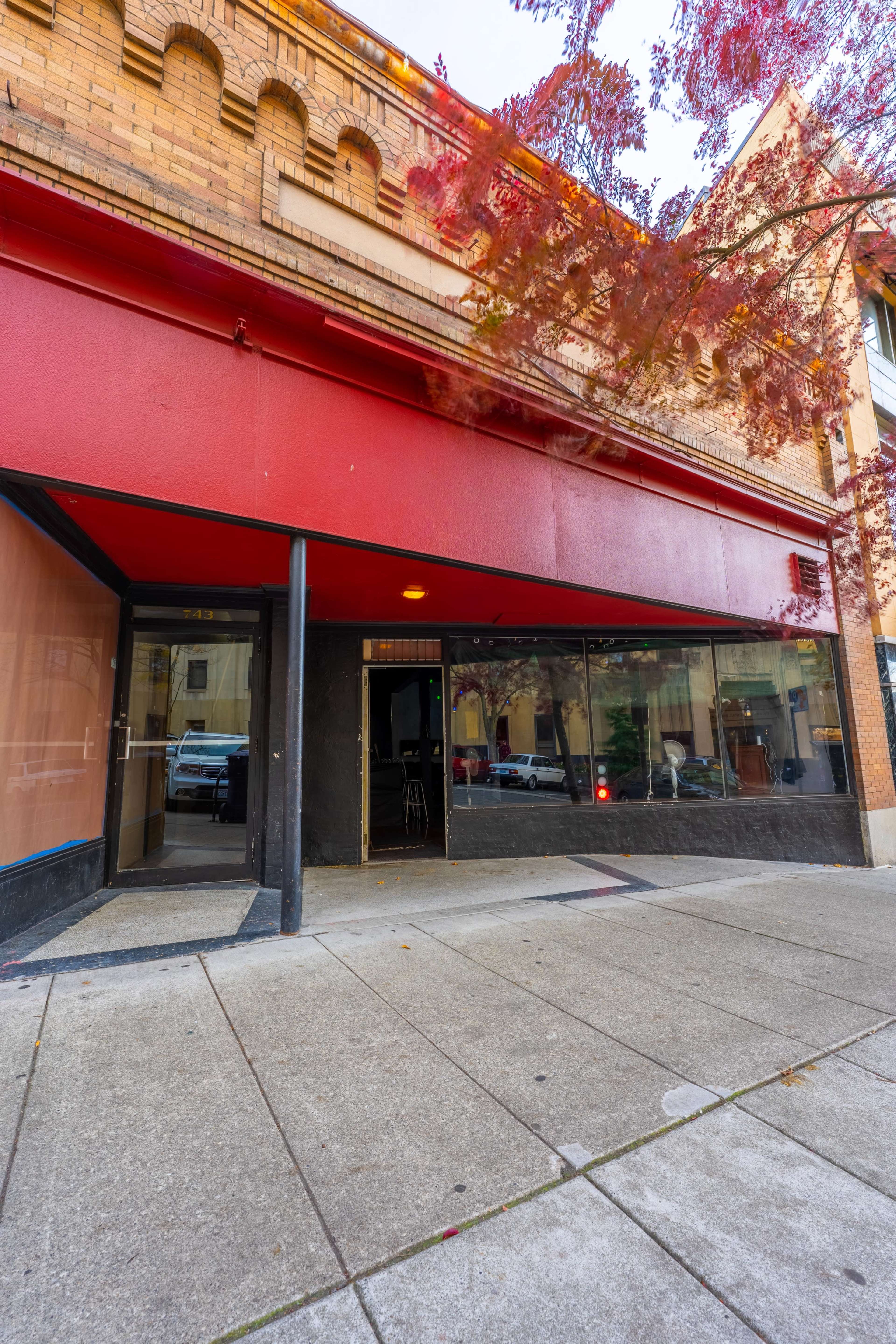 The exterior of a building featuring a red overhang and large glass windows on a sidewalk.