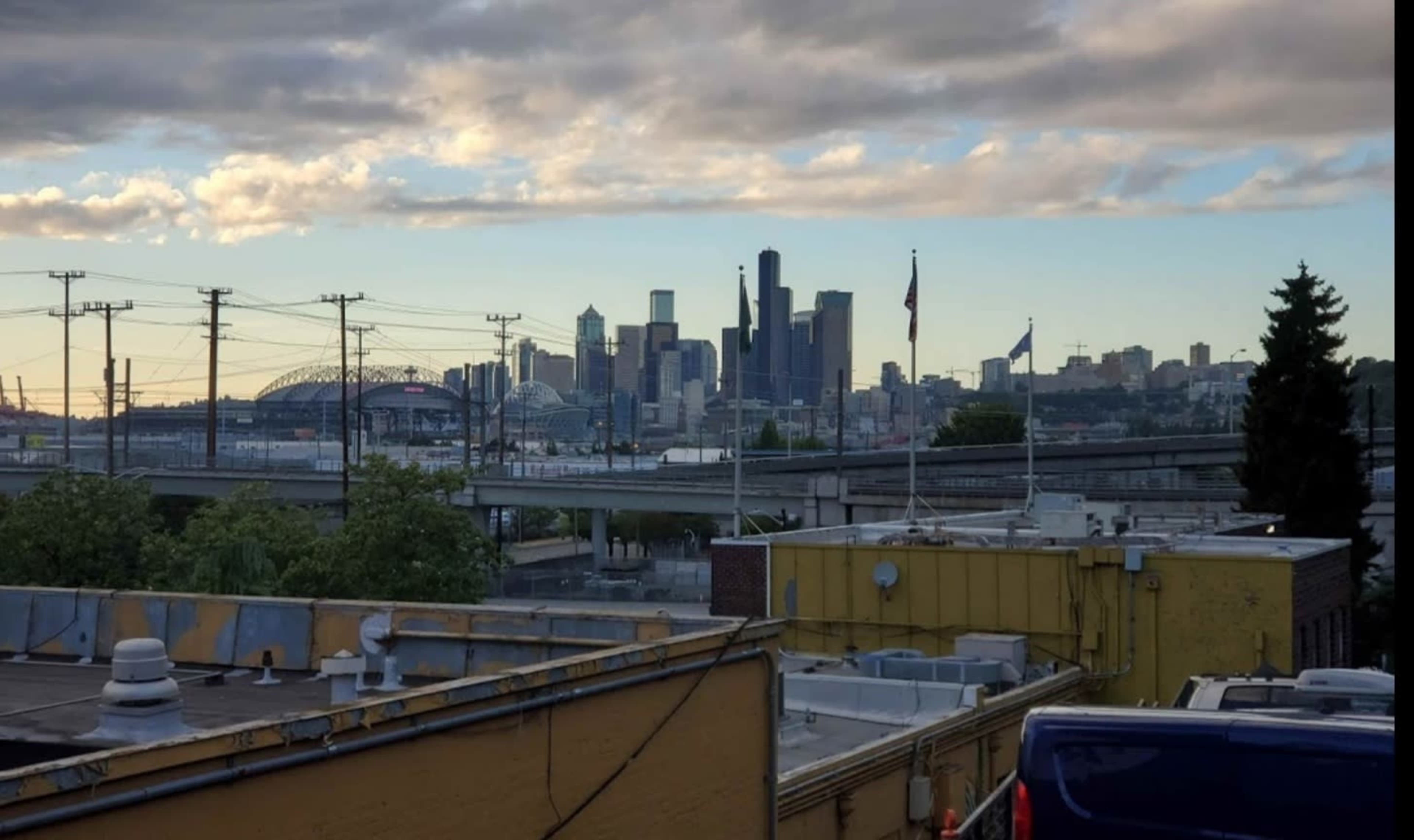 A view of the Seattle skyline with buildings, power lines, and a stadium in the background, taken from a rooftop vantage point.