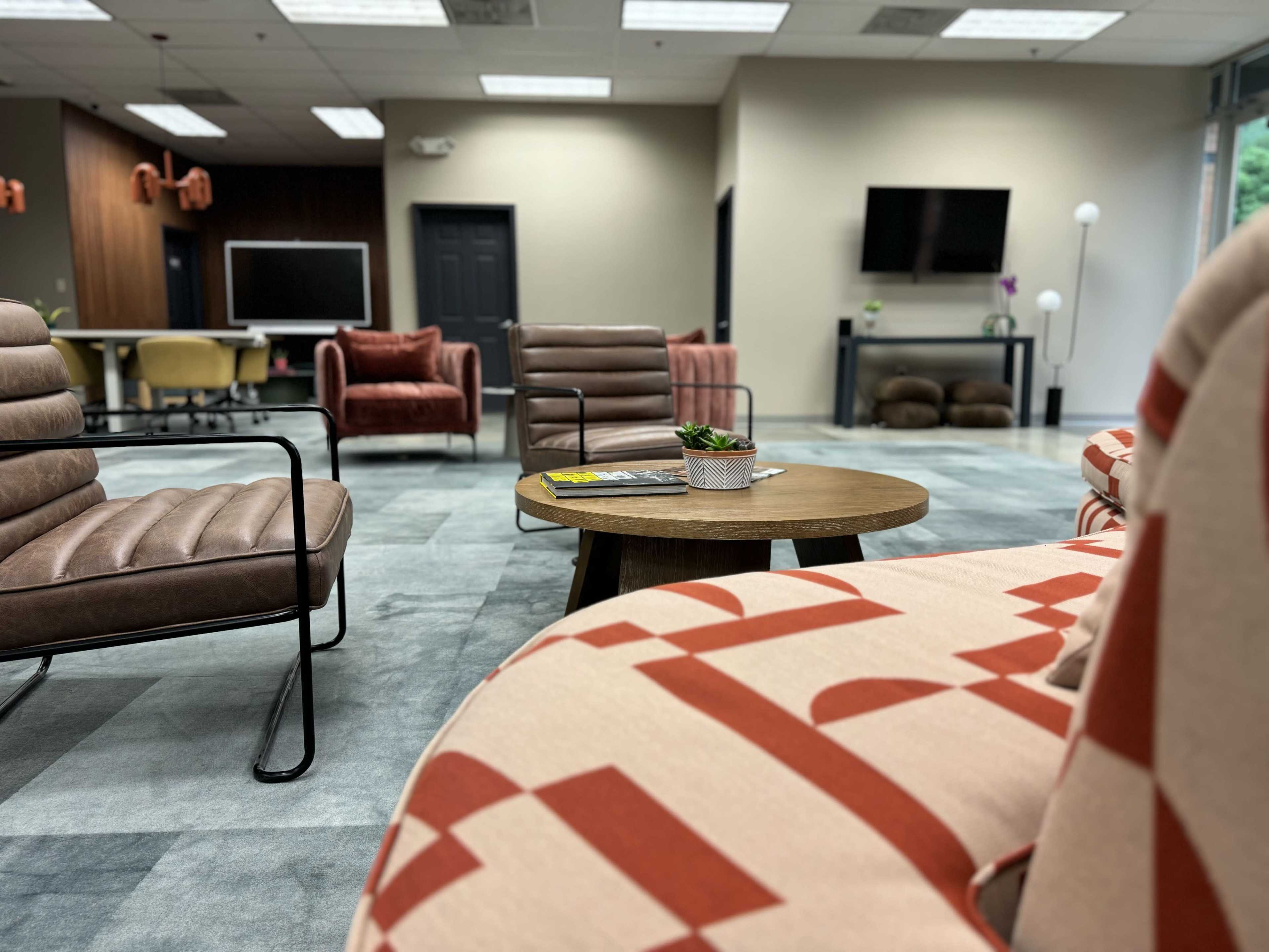 A modern lounge area features stylish seating in varied colors and a small wooden coffee table with a plant.