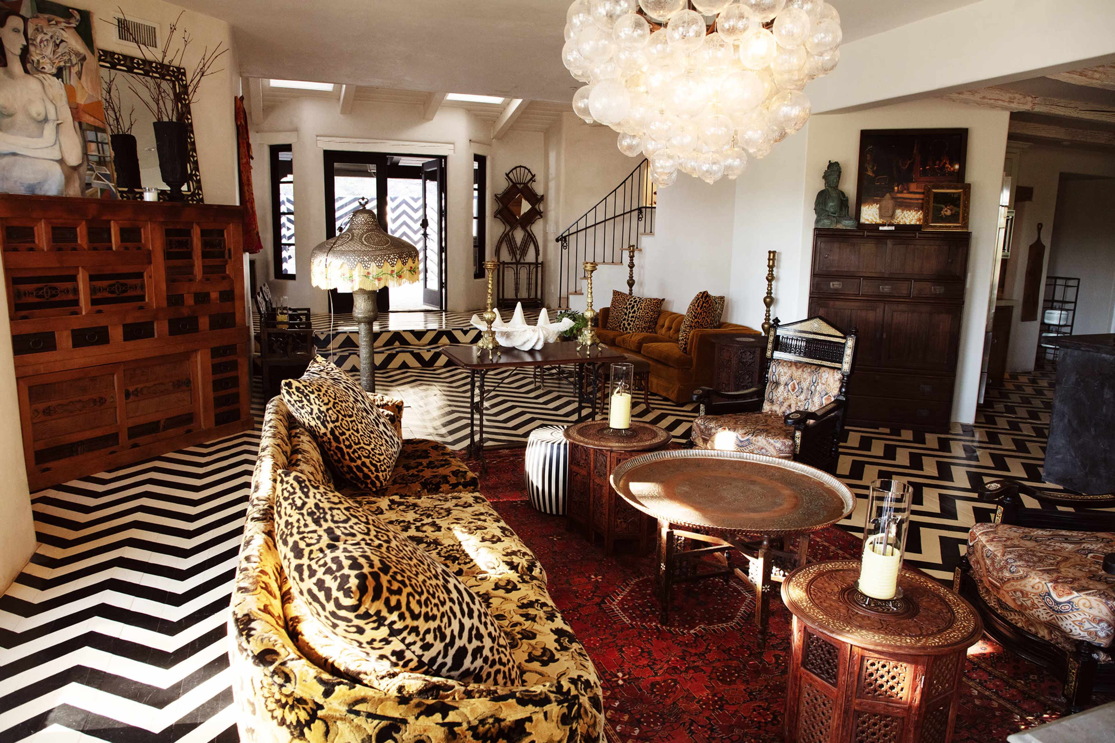The living room features a mix of patterned sofas, unique lighting fixtures, and an eclectic arrangement of furniture on a zigzag patterned floor.