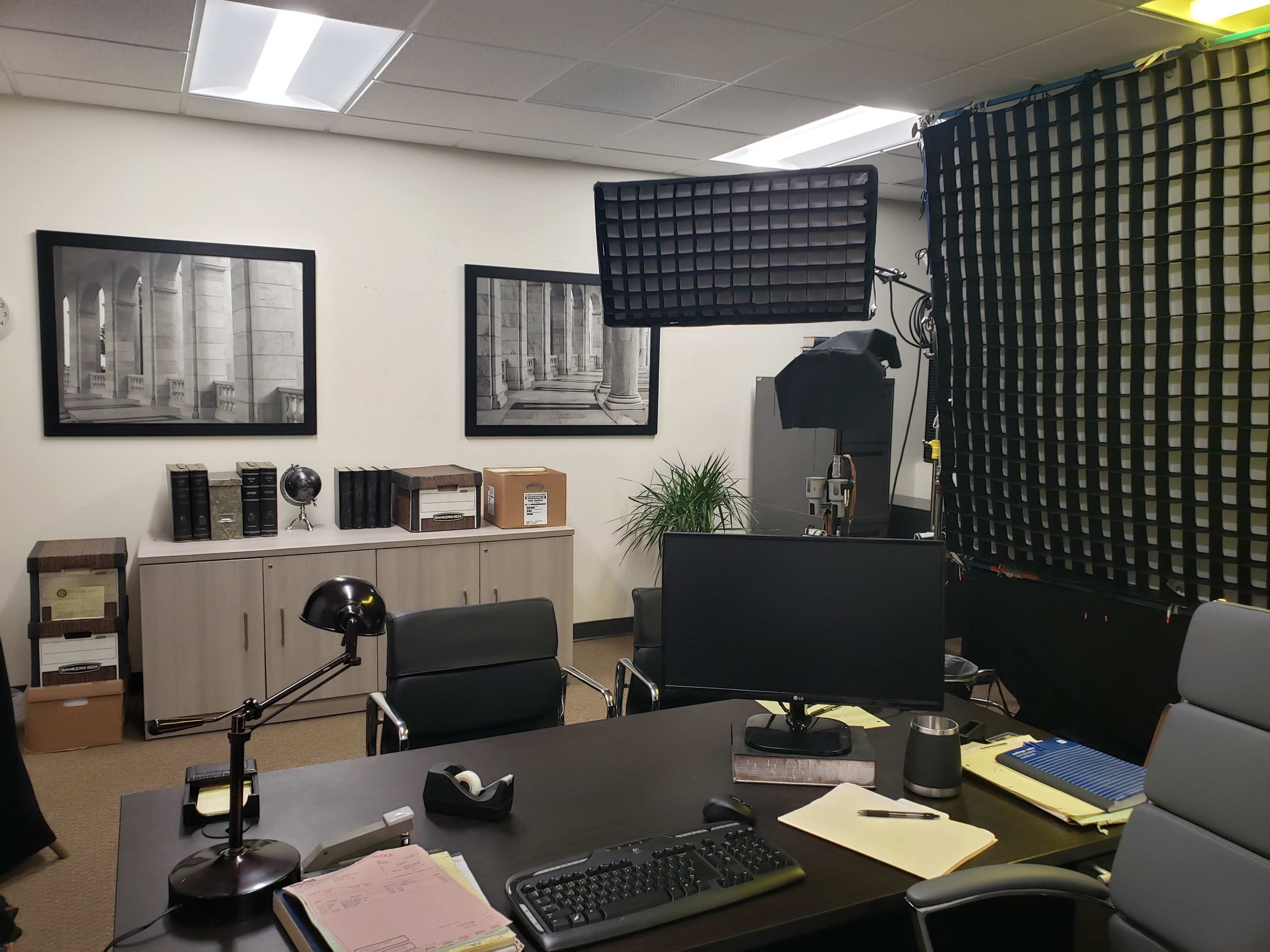 An office with a desk, computer, and large photographs on the walls, alongside shelves and various office equipment.