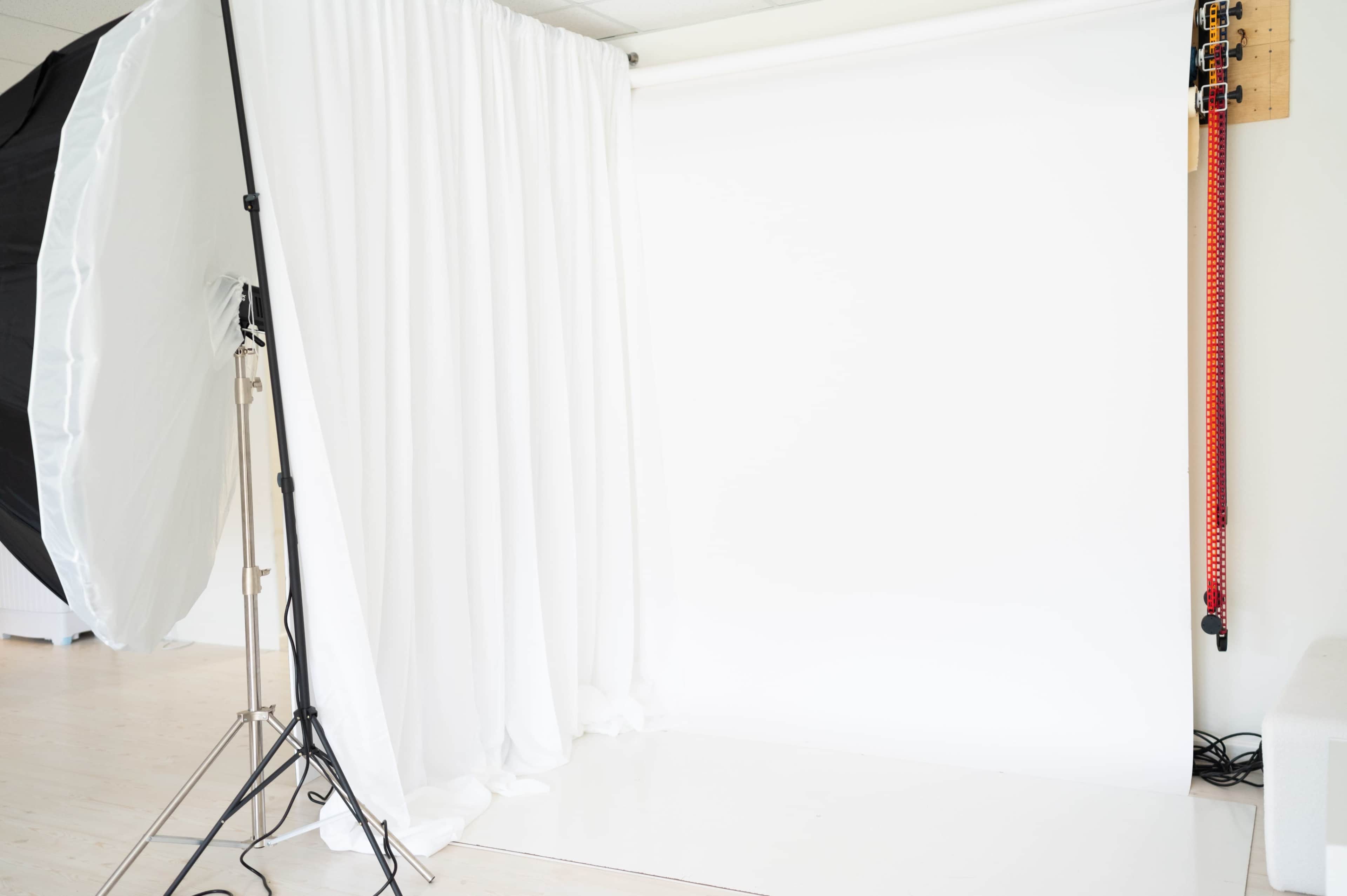 A photography studio features a large white backdrop draped on a stand, with additional lighting equipment nearby.