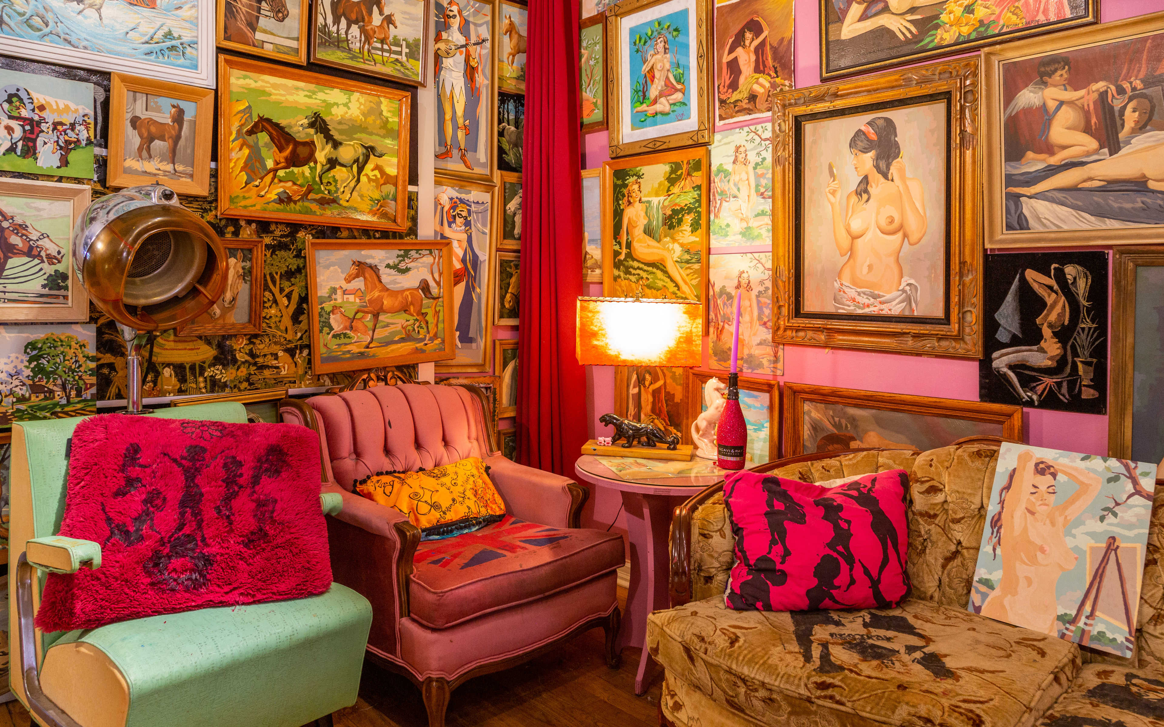 A cozy vintage-inspired sitting area filled with various framed artworks on the walls, including portraits and animal paintings, alongside brightly colored furniture.