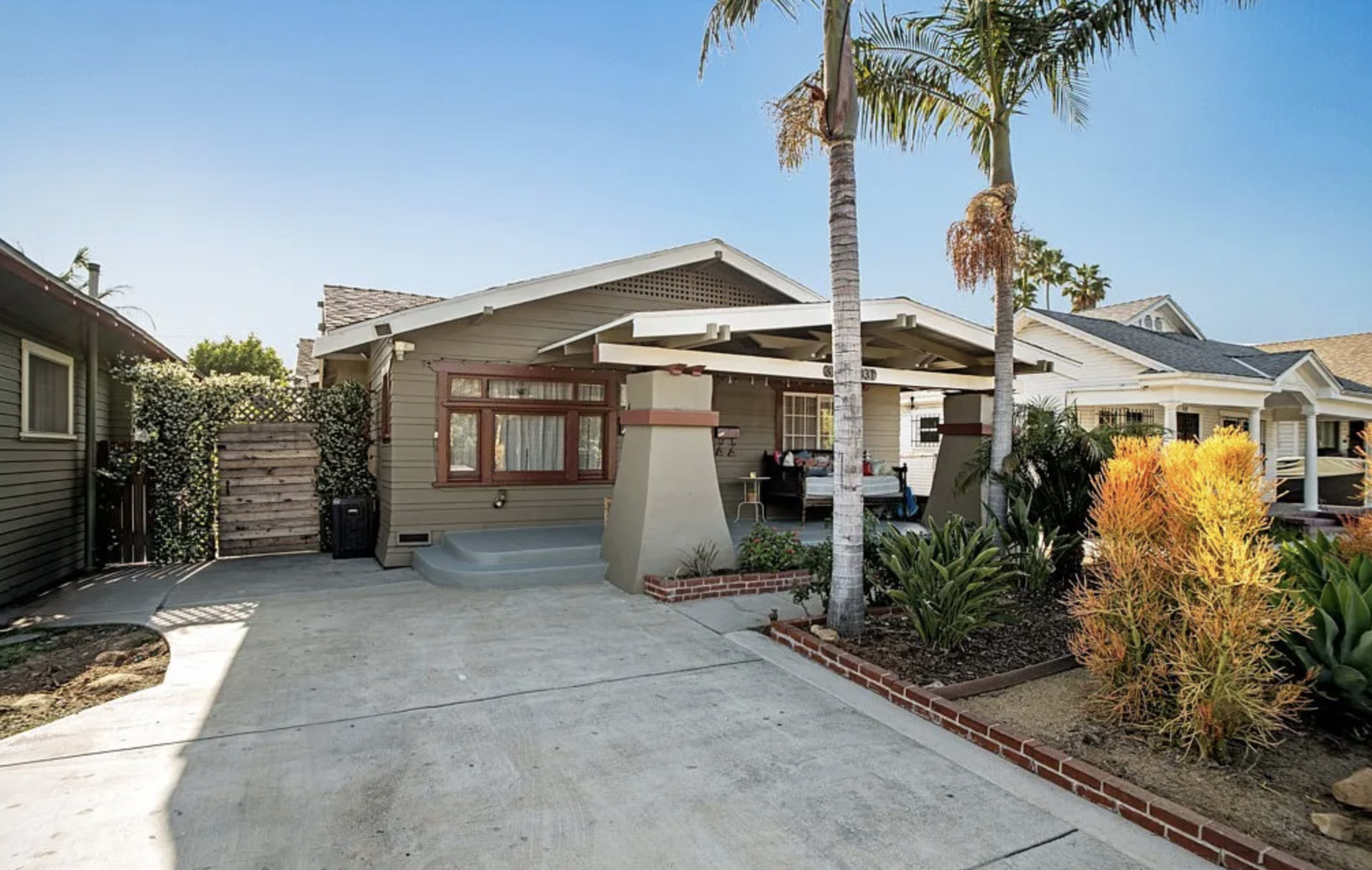 The image shows a single-story house with a covered patio, surrounded by palm trees and a landscaped yard.