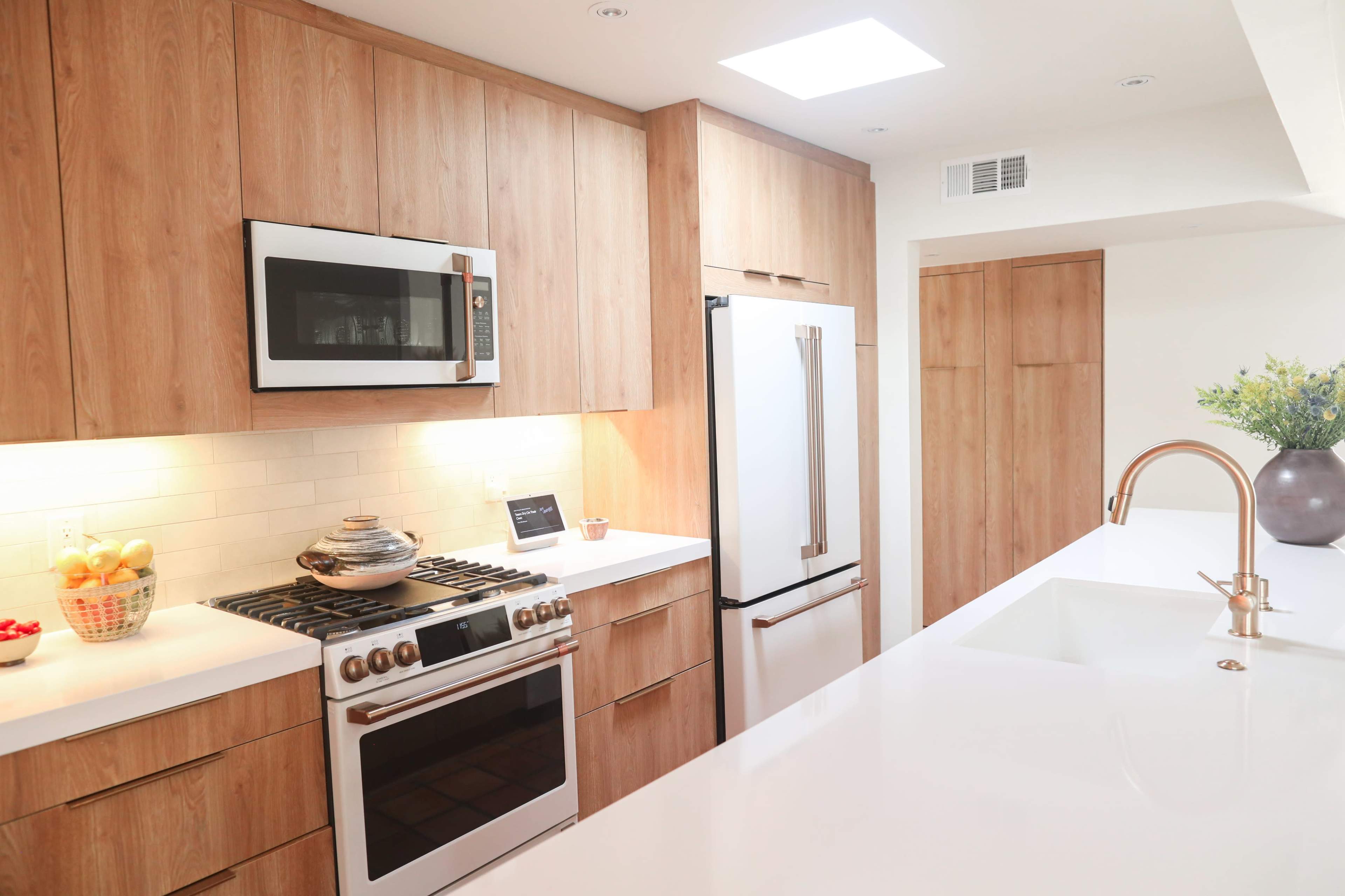 A modern kitchen features wooden cabinetry, stainless steel appliances, and a large white countertop with a sink.