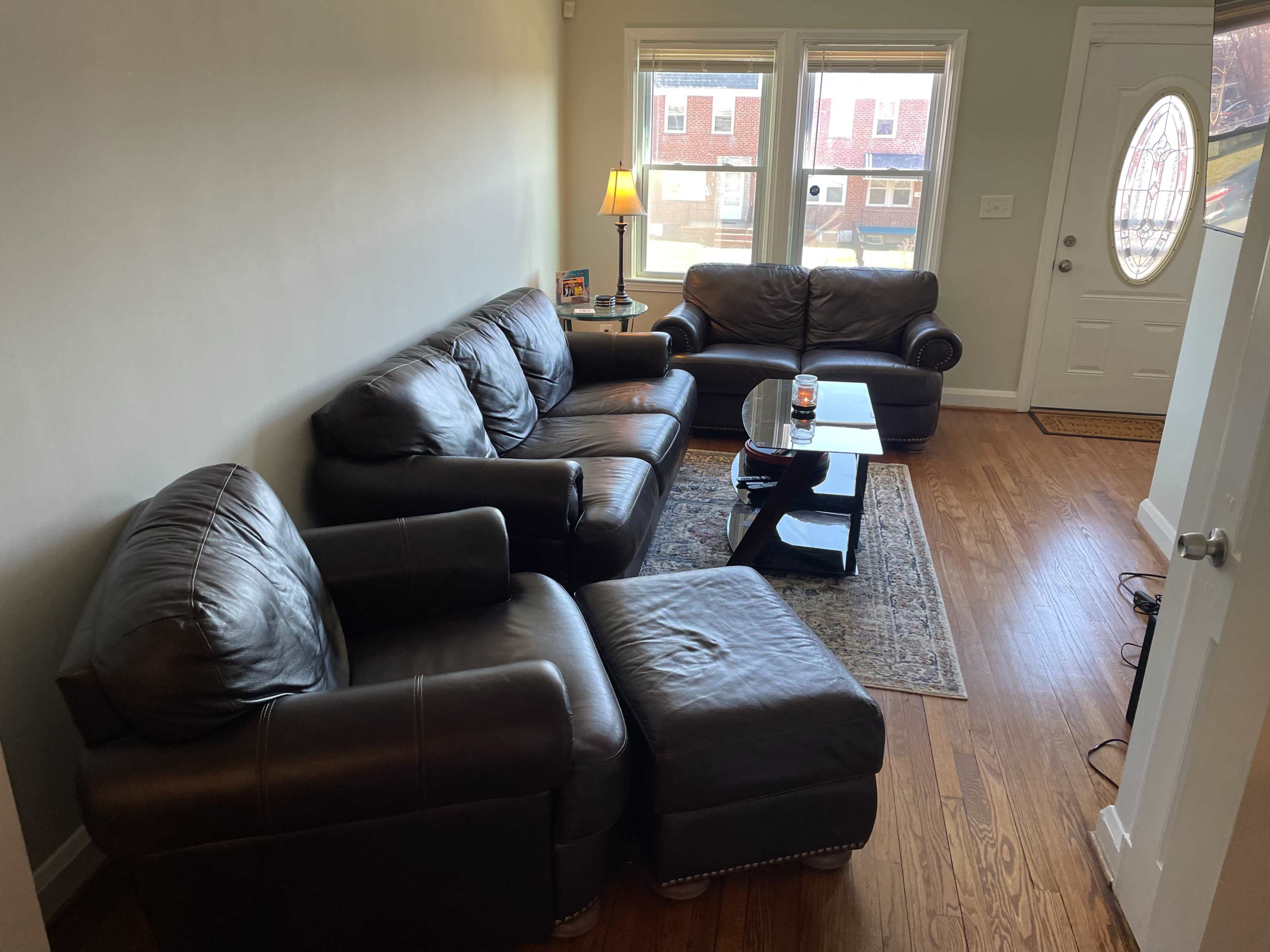A cozy living room with a dark leather seating arrangement, a coffee table, and a door leading outside.