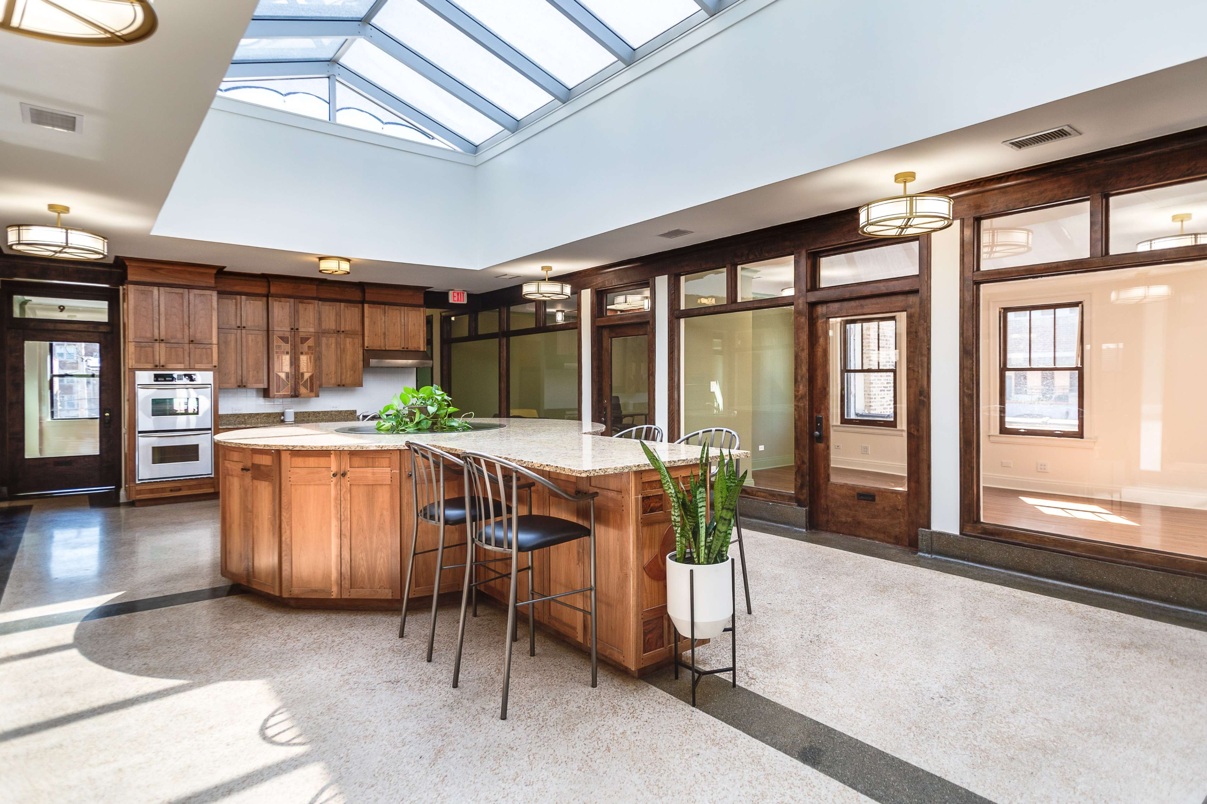 A spacious kitchen with a central island, wooden cabinetry, and large windows allowing natural light to enter.