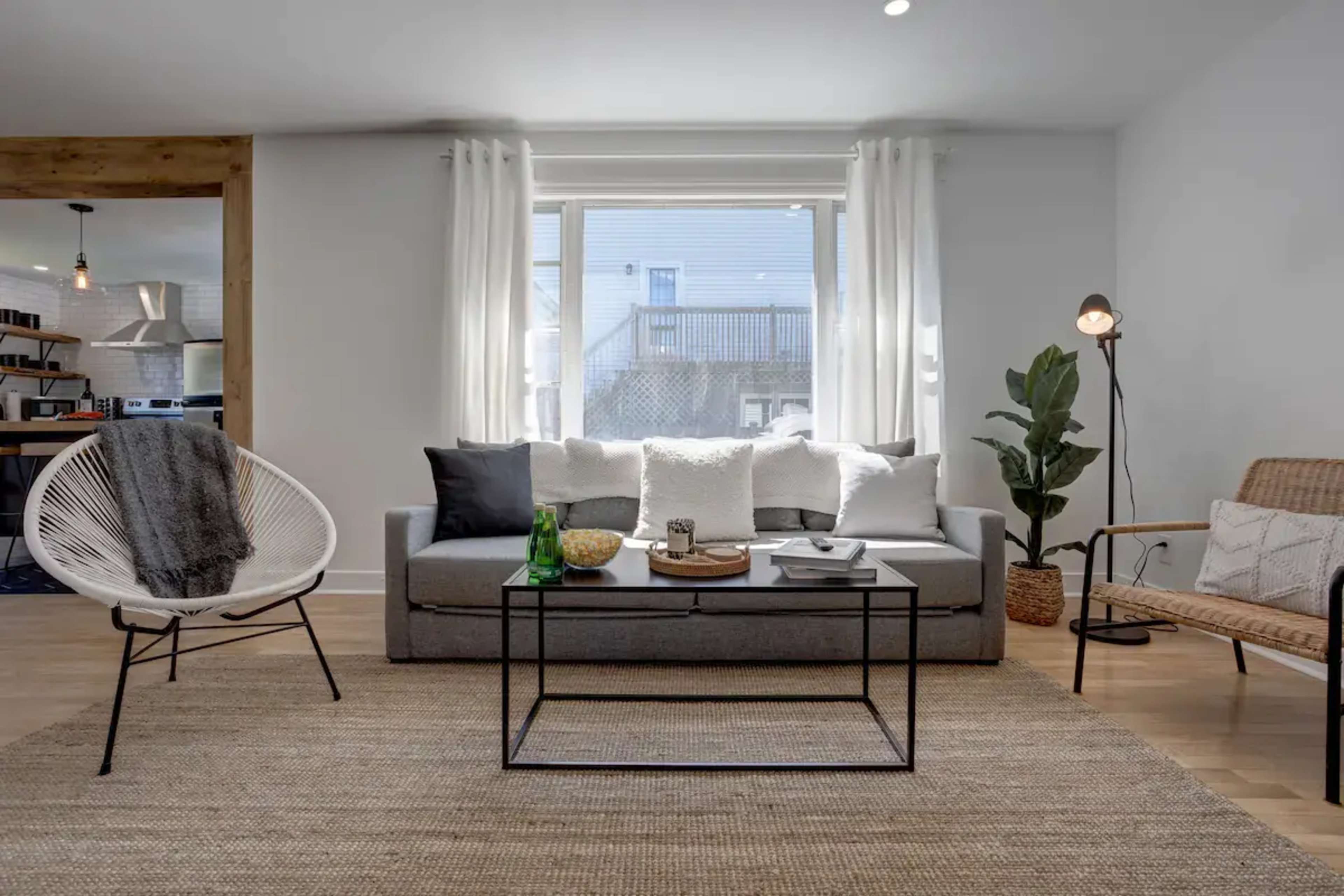 A modern living room with a gray sofa, a coffee table, and a chair, all arranged on a light-colored rug under natural light from a window.