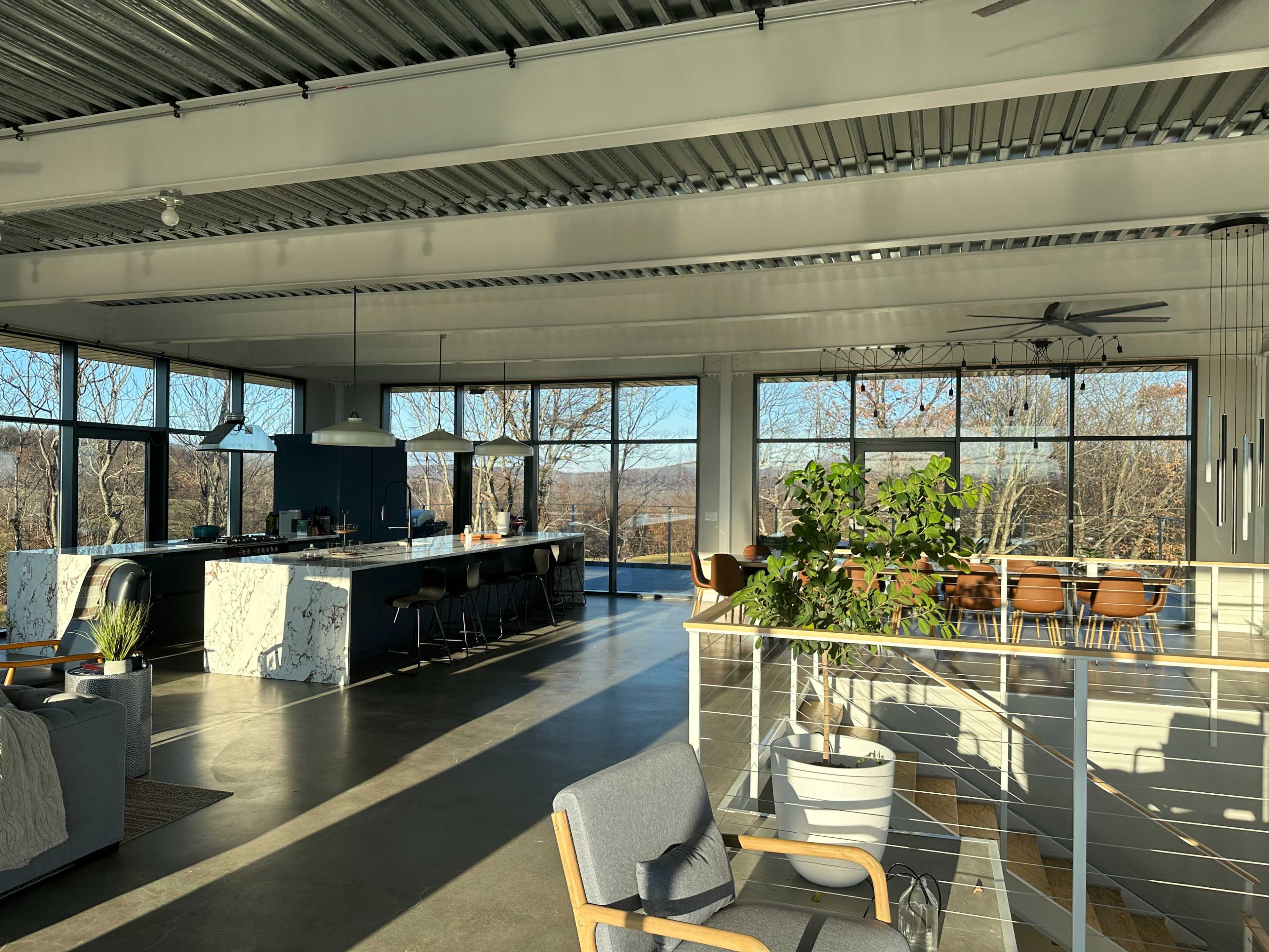 A spacious modern interior featuring a kitchen and dining area with large windows overlooking a natural landscape.