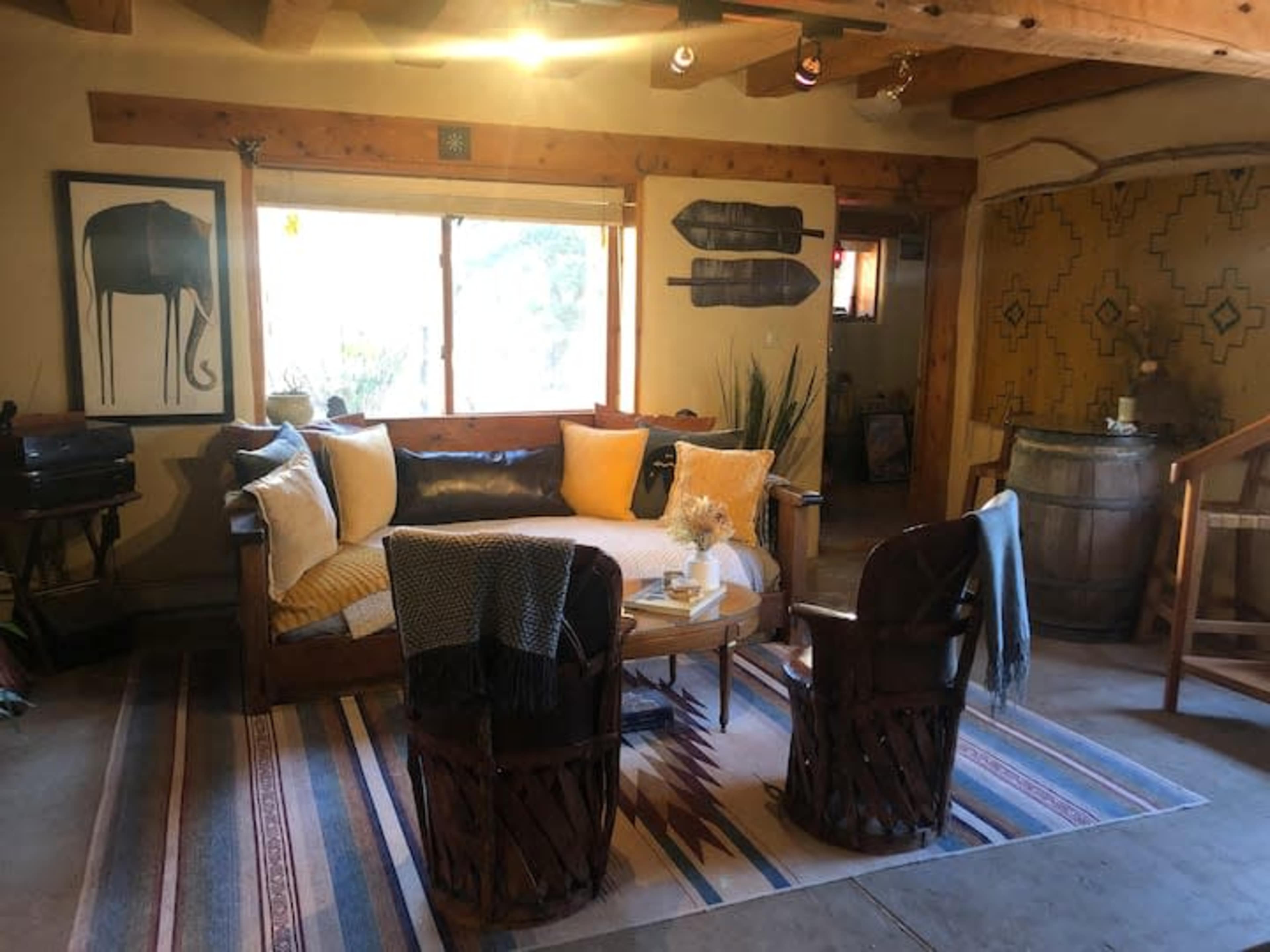 A cozy living room with a wooden sofa adorned with cushions, two woven chairs, a coffee table, and decorative Native American-inspired wall art.