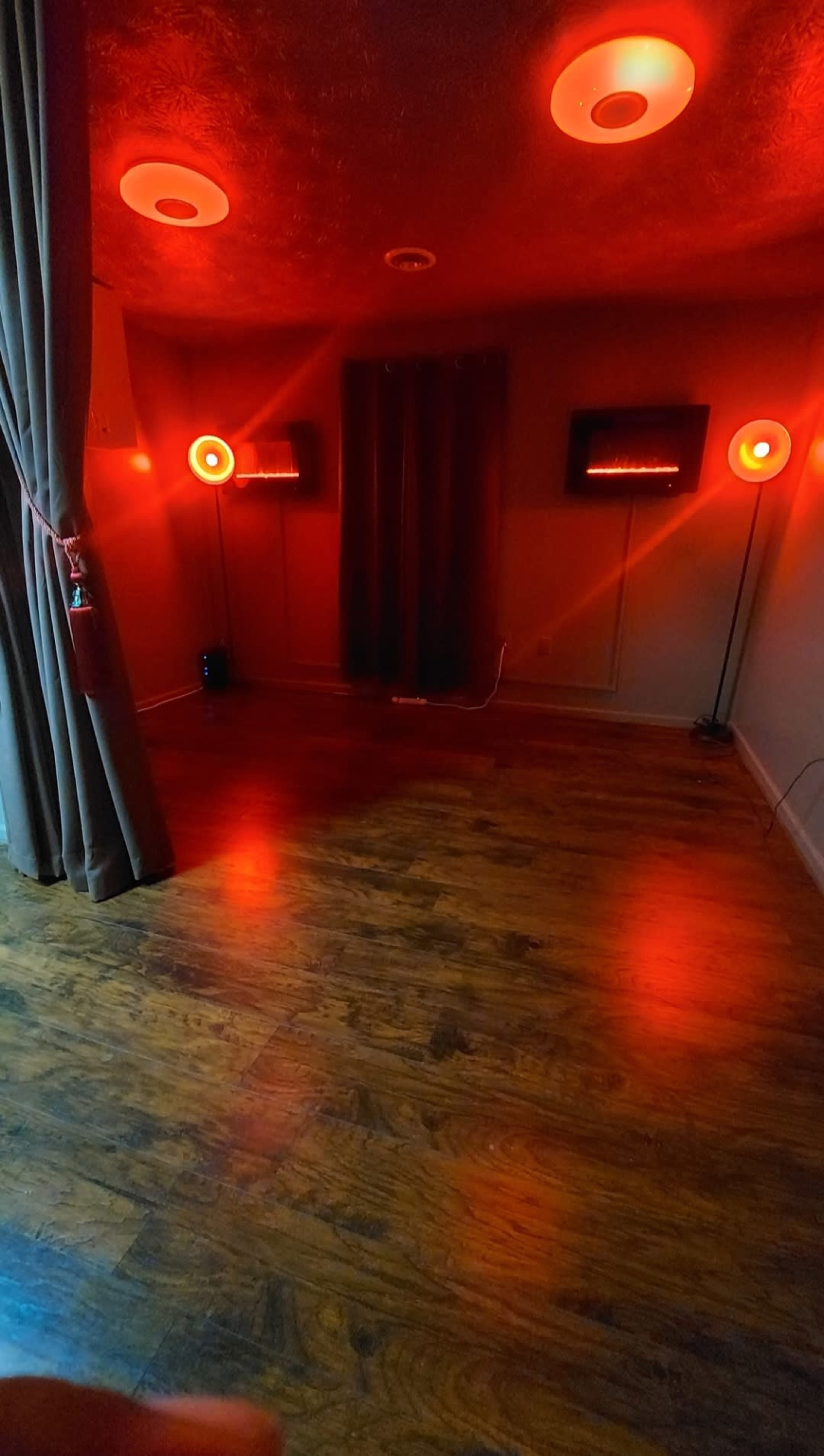 The room features hardwood flooring, two red lamps on stands, and dark curtains, creating a dimly lit environment.