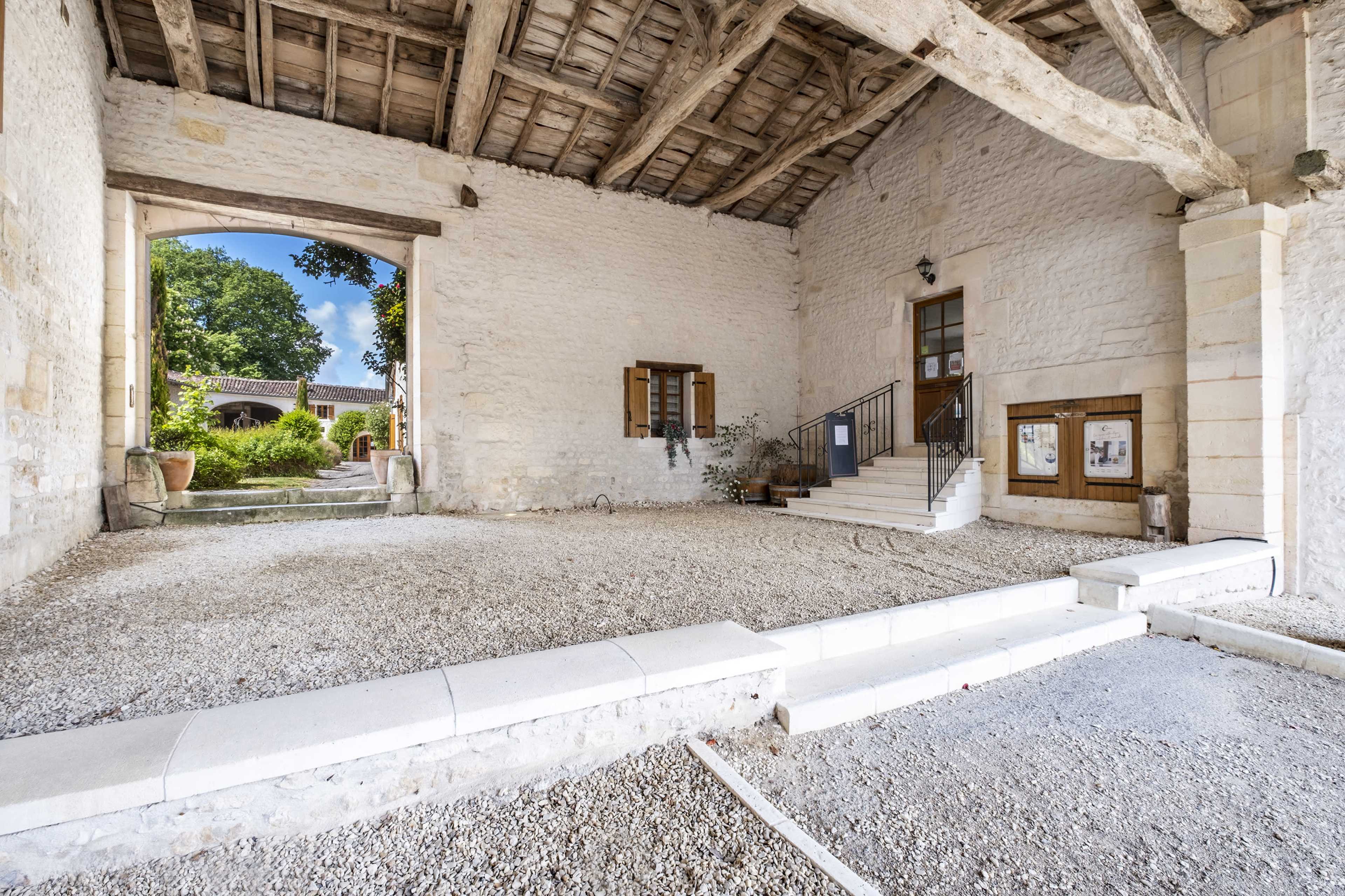 The image shows a spacious, stone-walled area with a wooden ceiling, featuring steps leading to a doorway and several windows.