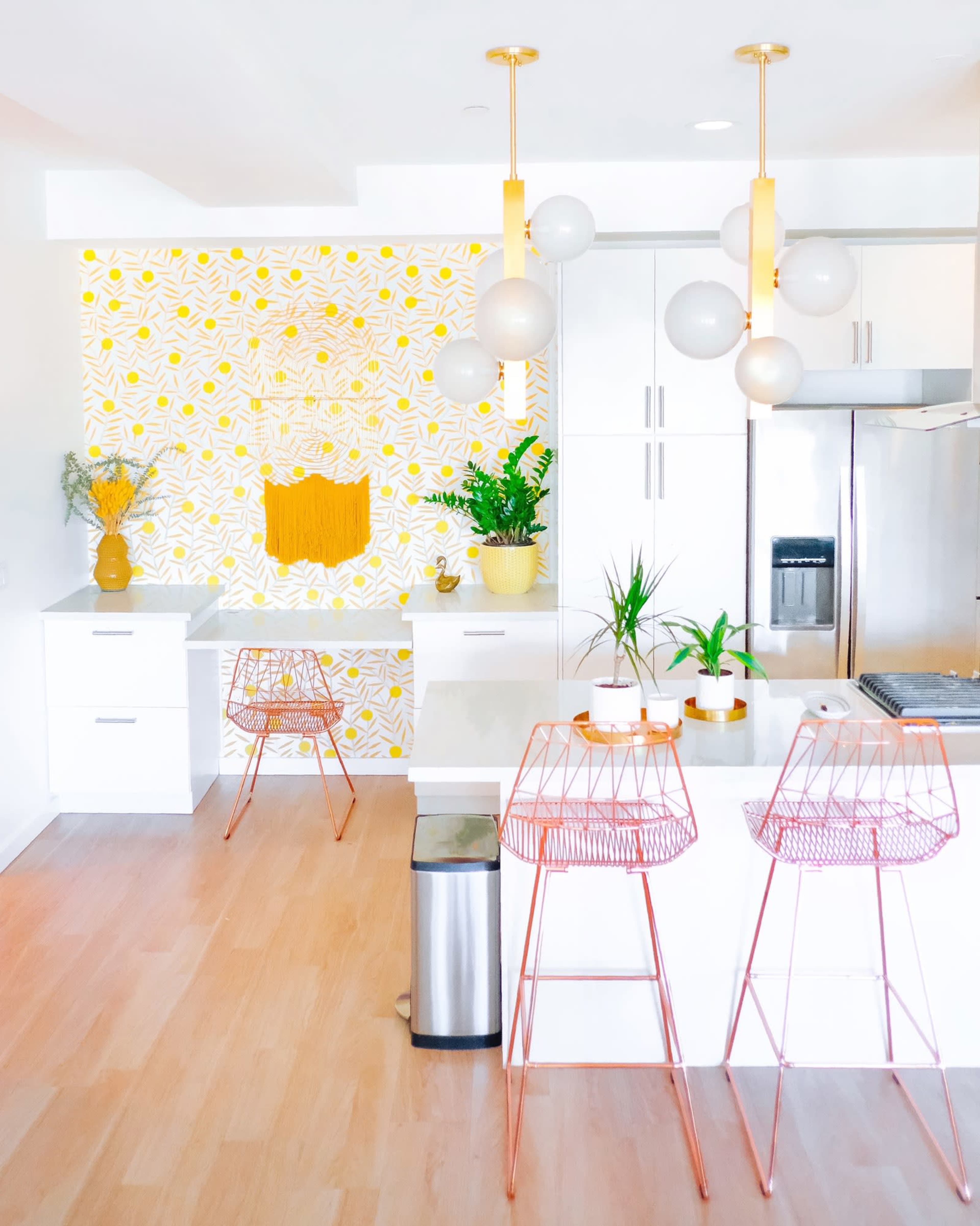 A modern kitchen features white cabinetry, a patterned yellow accent wall, and copper bar stools around a central island.