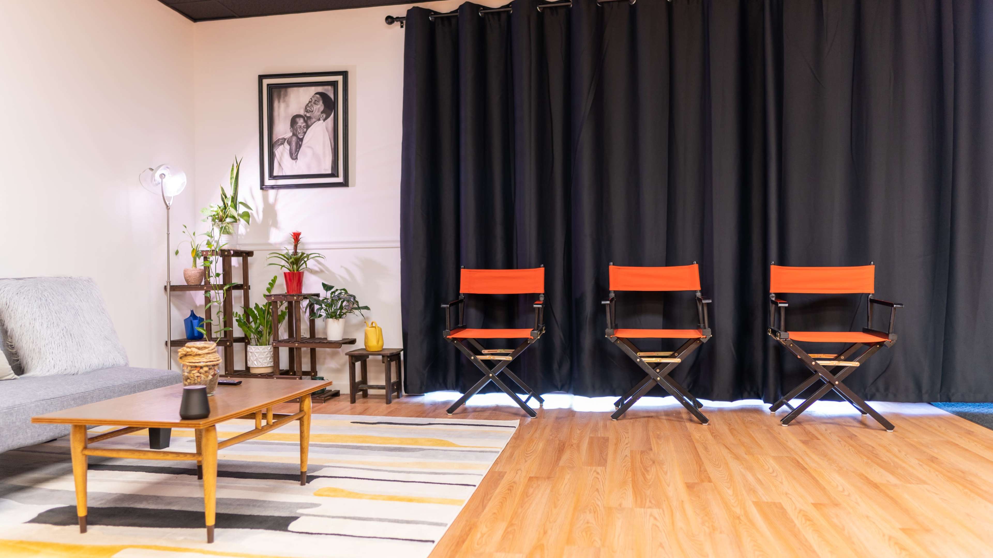 A cozy interior with a gray sofa, a coffee table, three red director's chairs, and a black curtain backdrop.