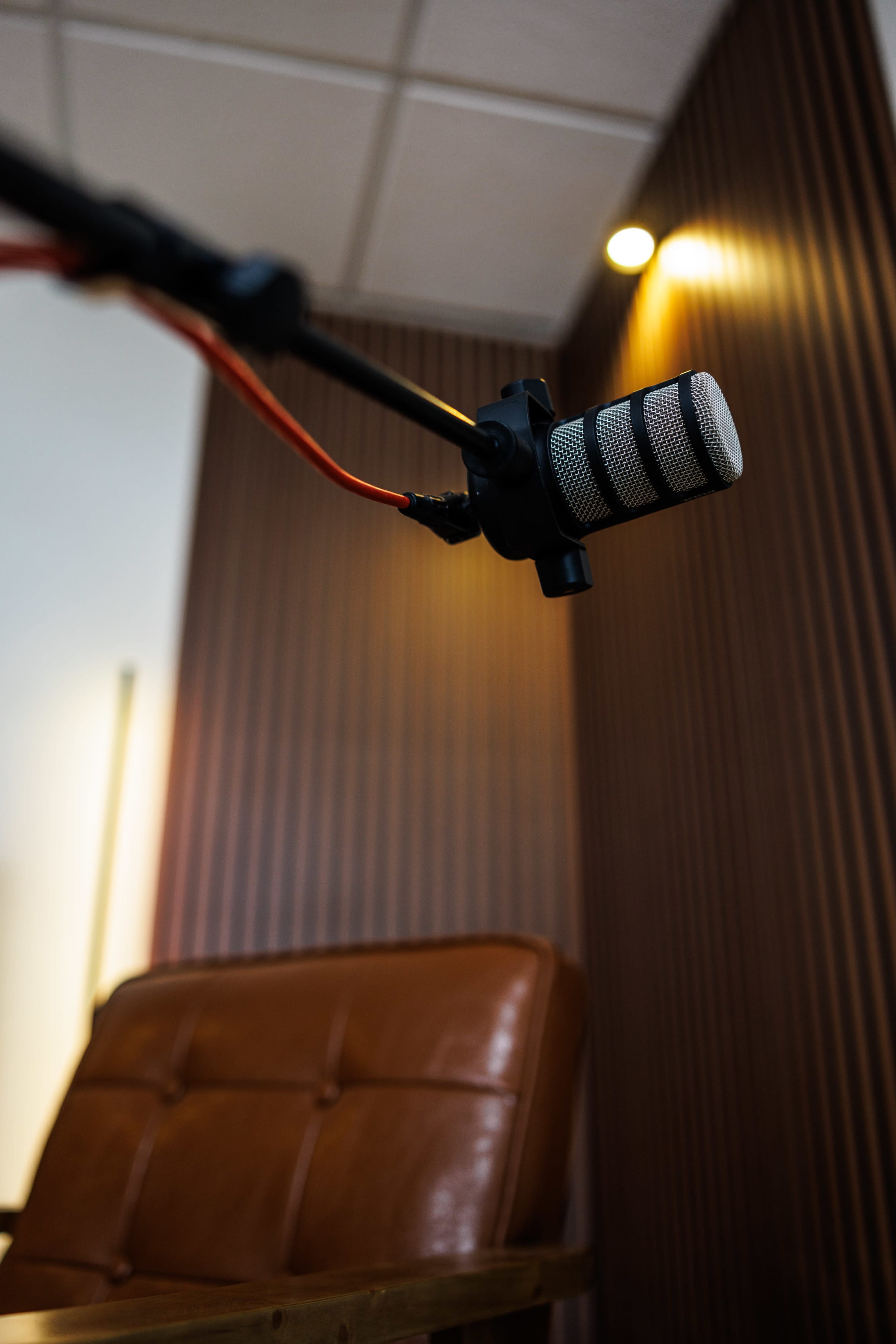 A close-up of a microphone mounted on a stand, positioned in front of a brown leather chair against a backdrop of wooden paneling and soft lighting.