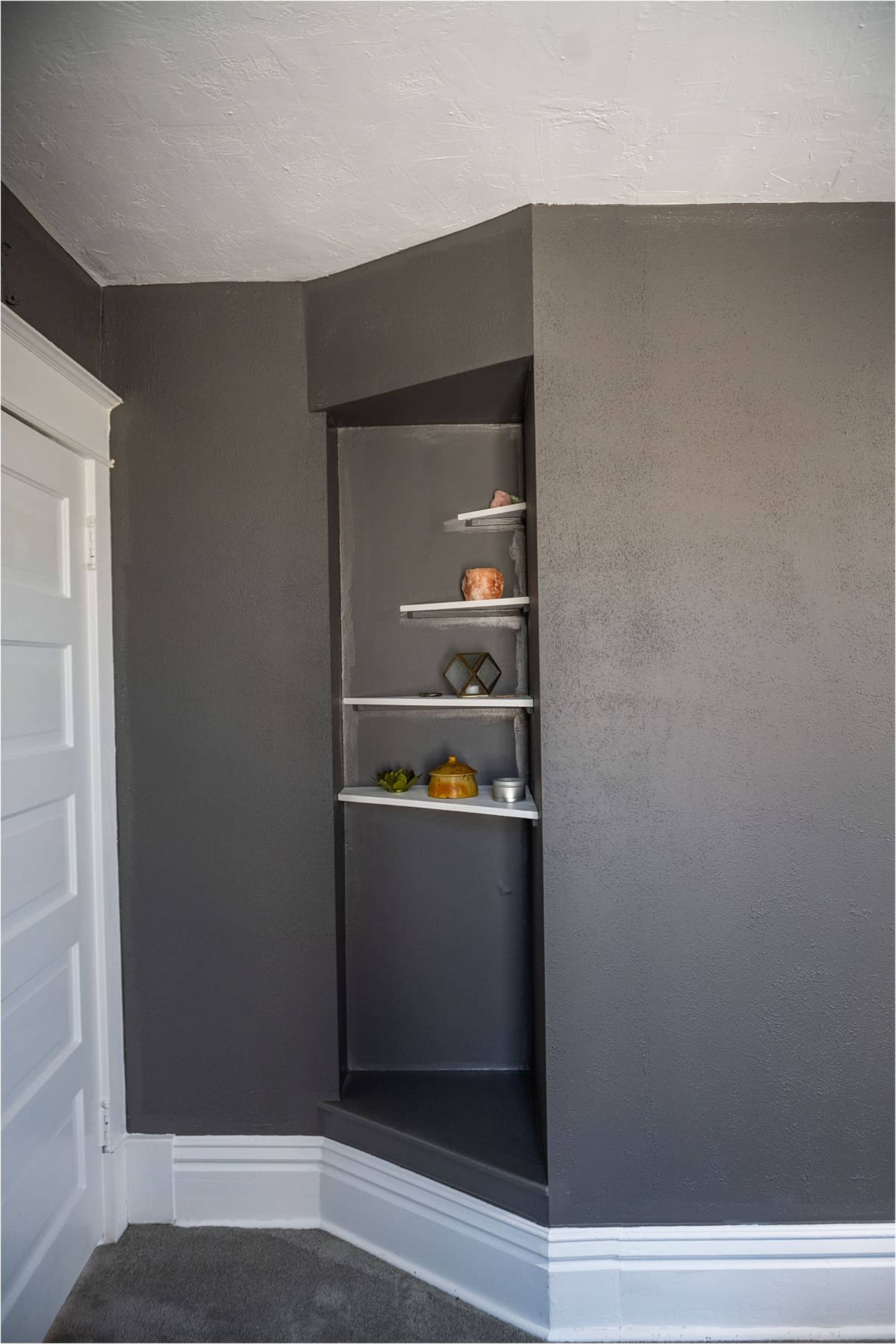 A small, gray alcove in a corner with five shelves displaying various decorative items.
