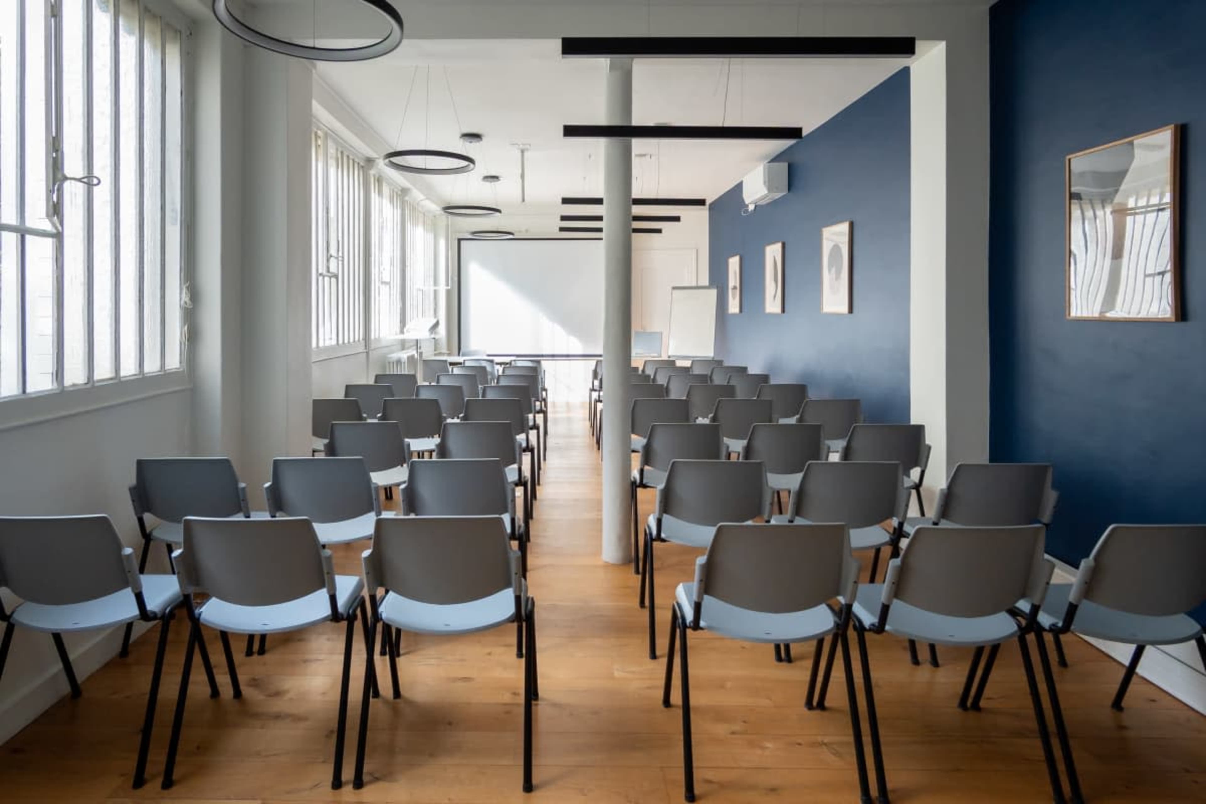 A conference room is arranged with rows of chairs facing a projection screen on a wall.