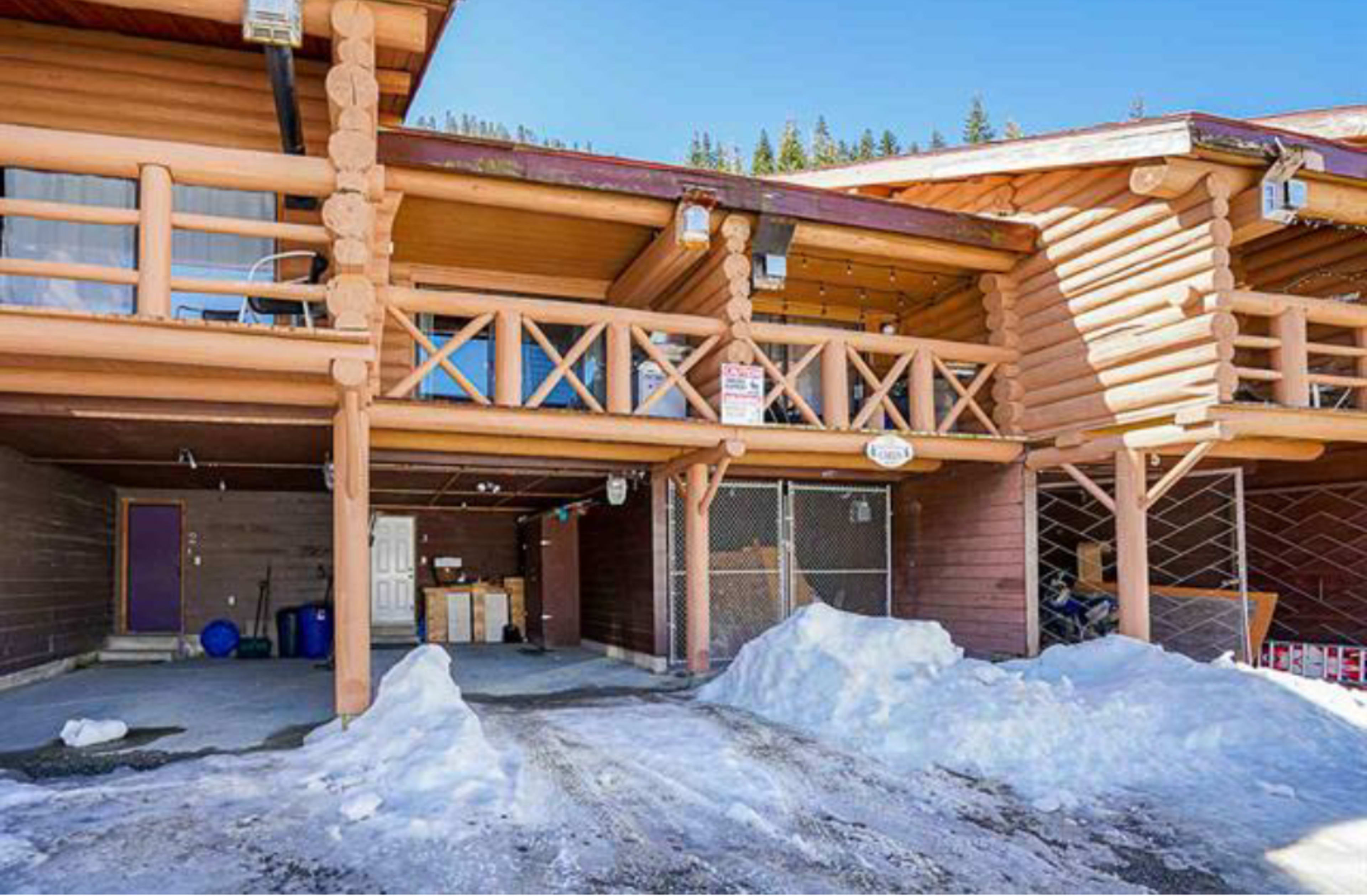 A log cabin-style building with a snow-covered driveway and covered parking area.