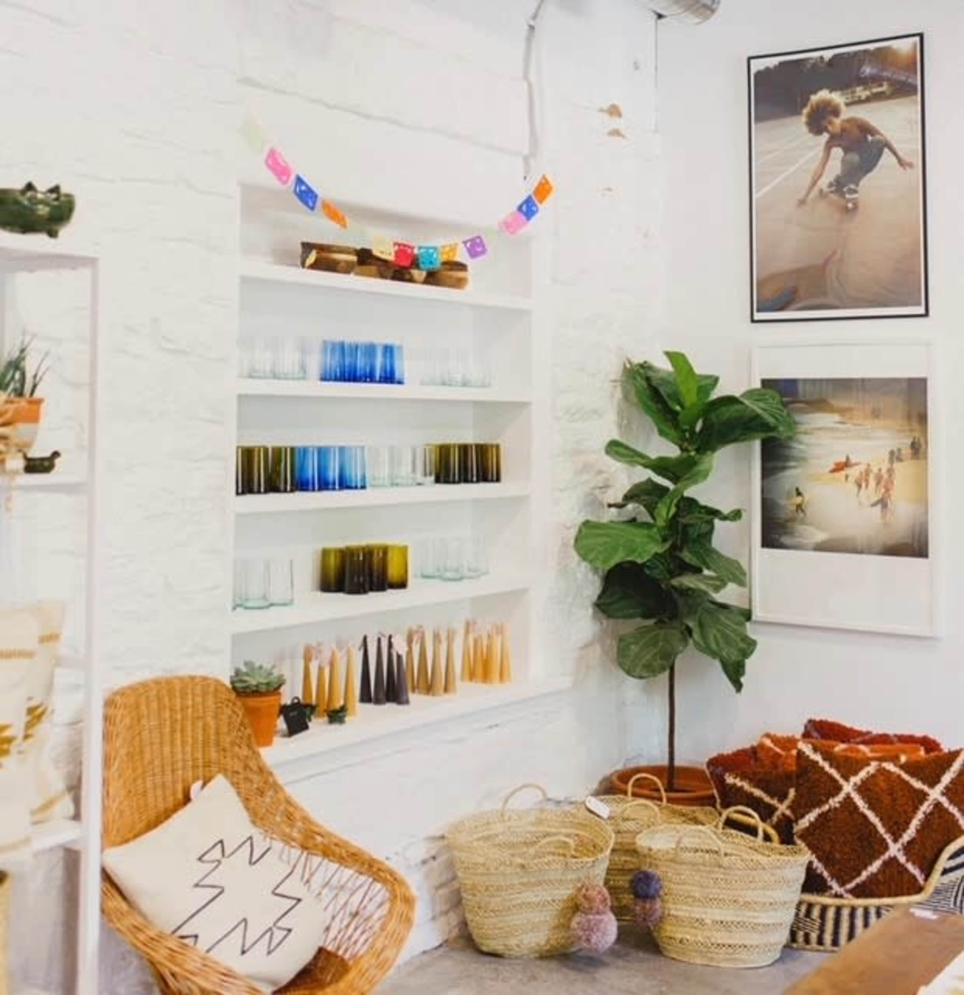 A cozy corner of a store featuring shelves of colorful glassware, decorative photos on the wall, plants, and woven baskets.