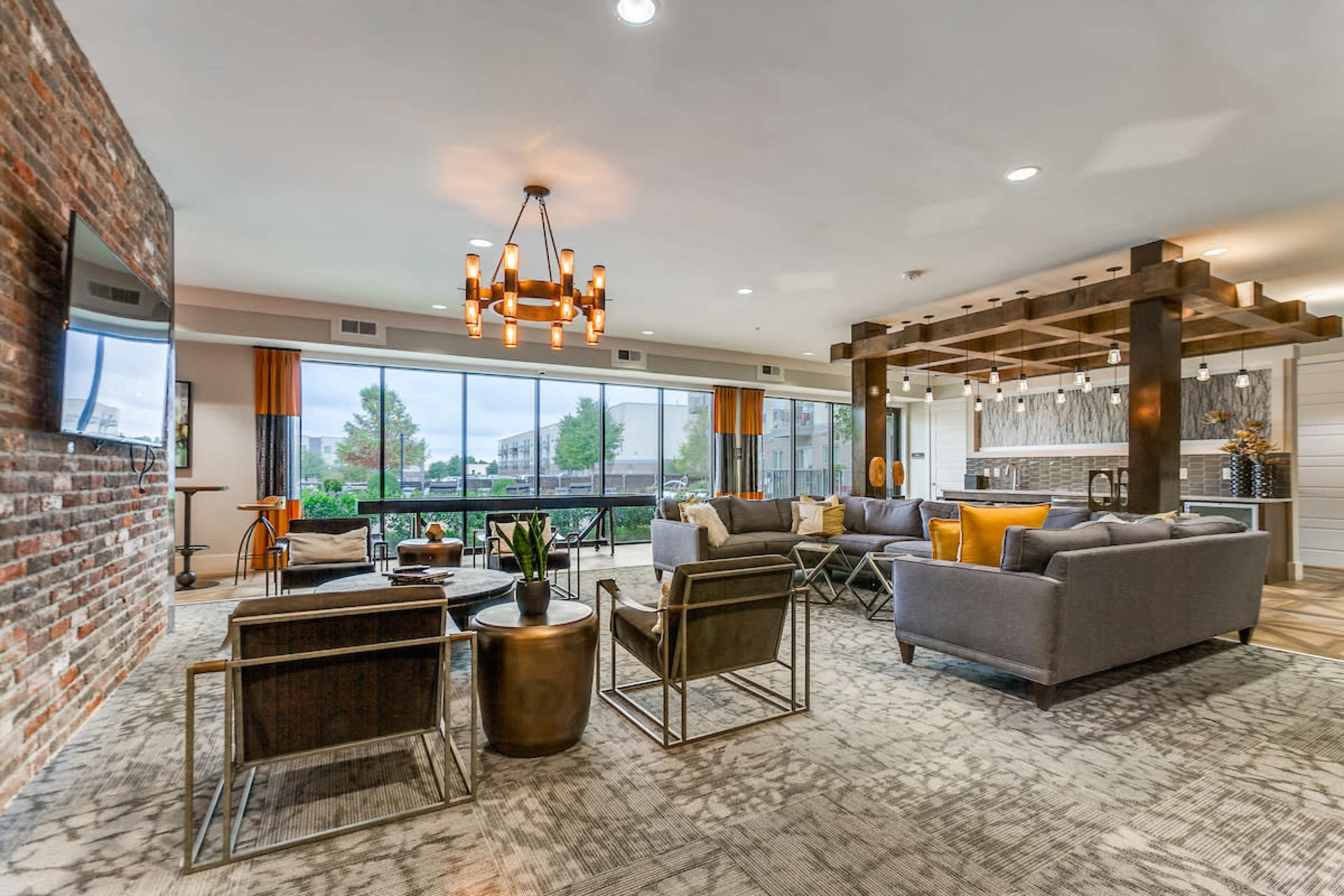 A modern living area featuring exposed brick walls, large windows, and stylish furniture arranged around a central coffee table.