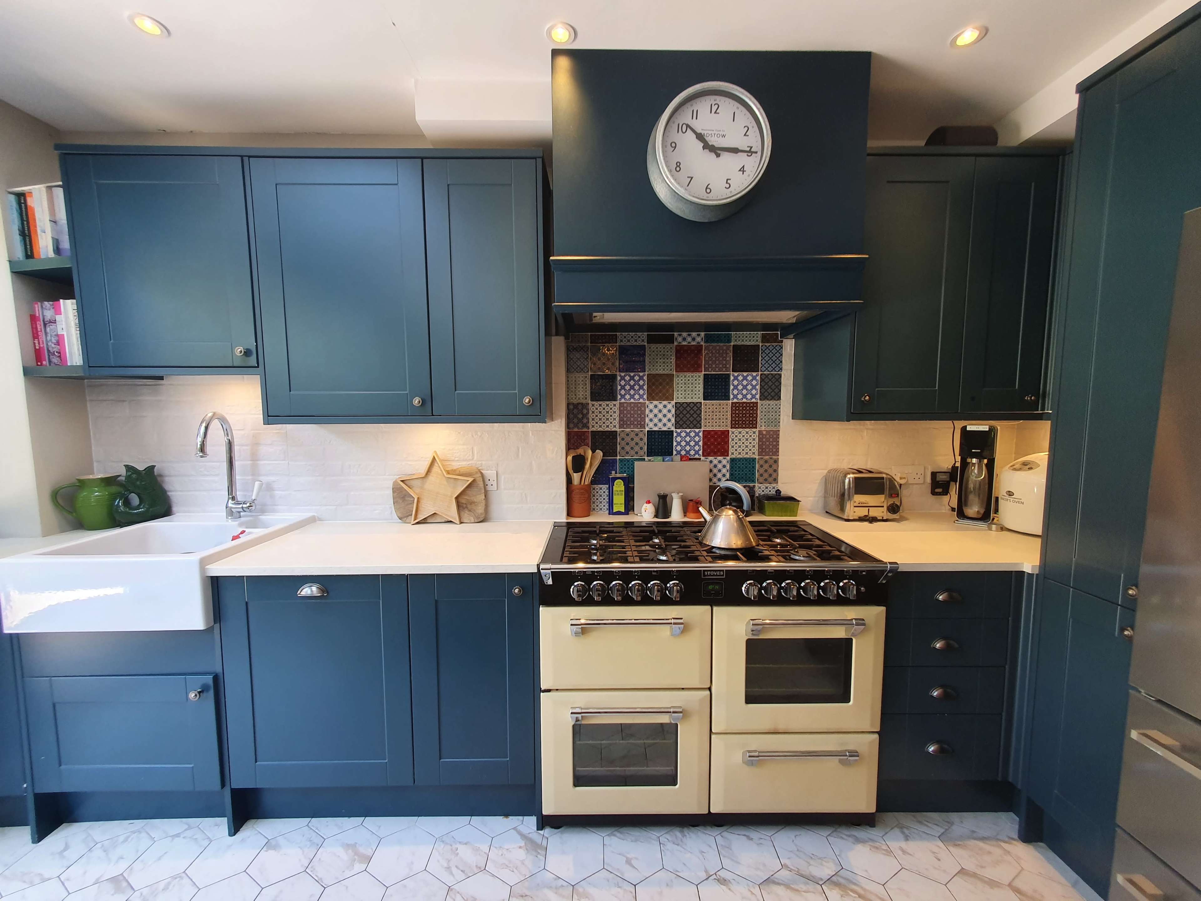 The kitchen features blue cabinetry, a gas range with a cream-colored finish, and a tiled backsplash with a mix of red and blue patterns.