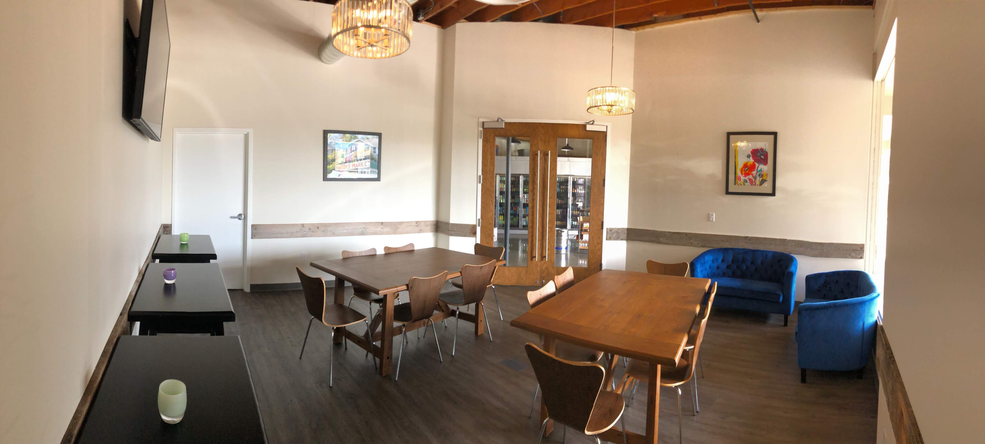 A modern meeting room with wooden tables, chairs, and a blue sofa, illuminated by chandelier lighting.