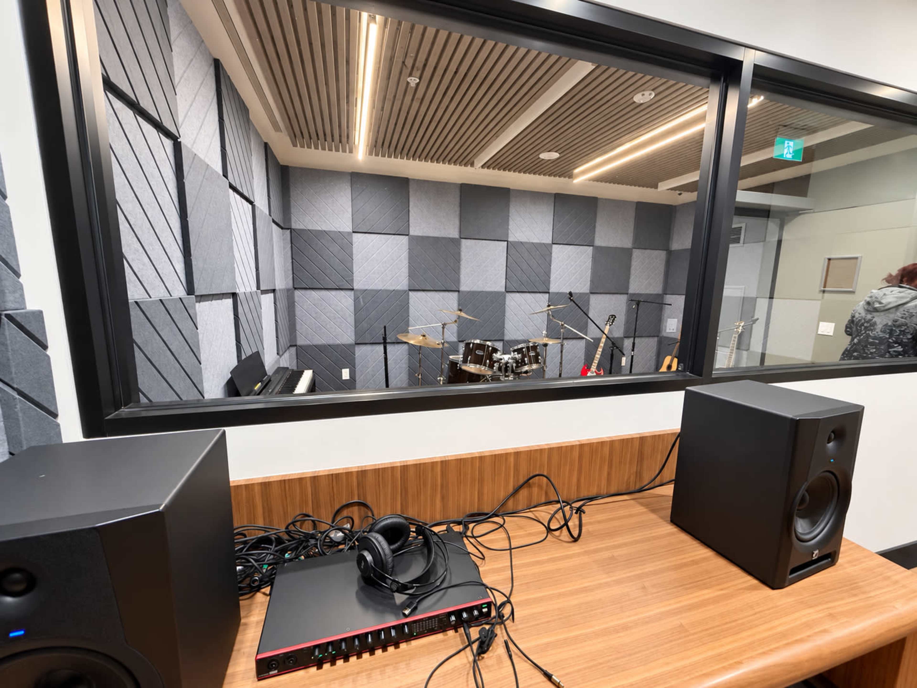 The image shows a recording studio with soundproofed walls, visible musical instruments, and audio equipment in the foreground.