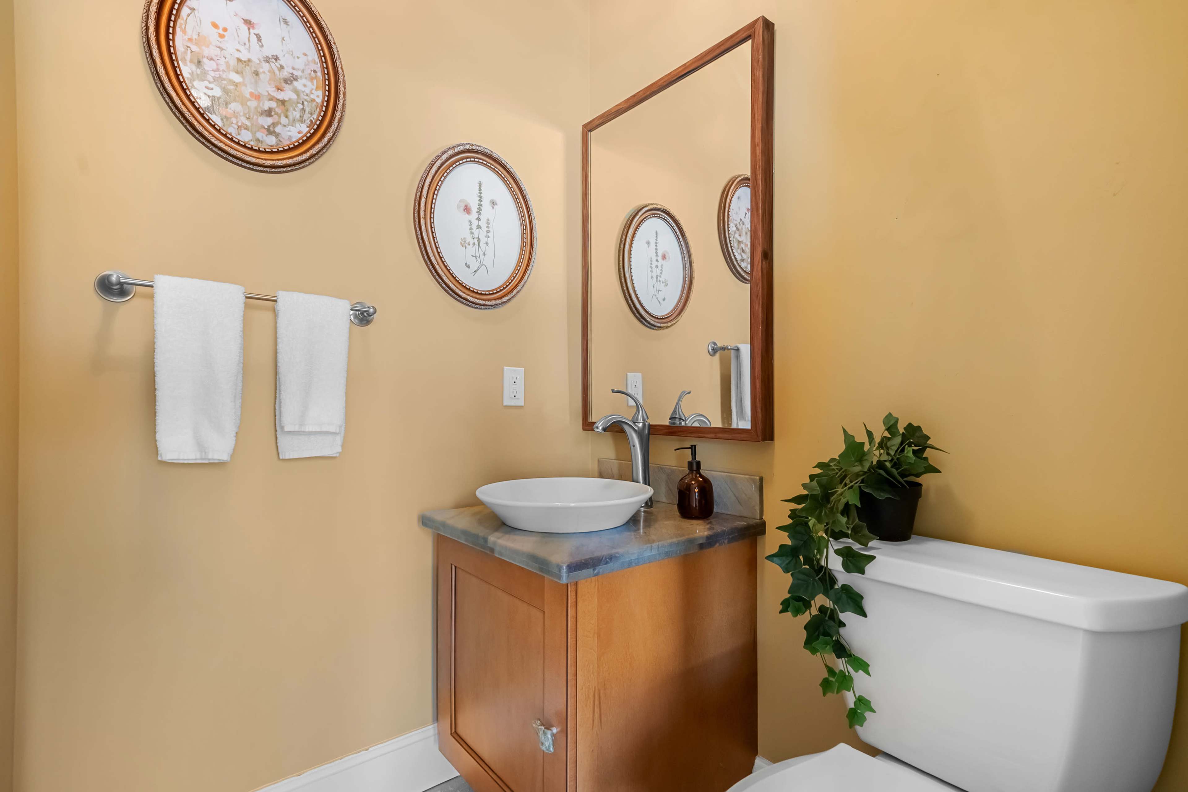 The image shows a small bathroom with a yellow wall, a mirror above a sink, a wooden cabinet, and a white toilet.