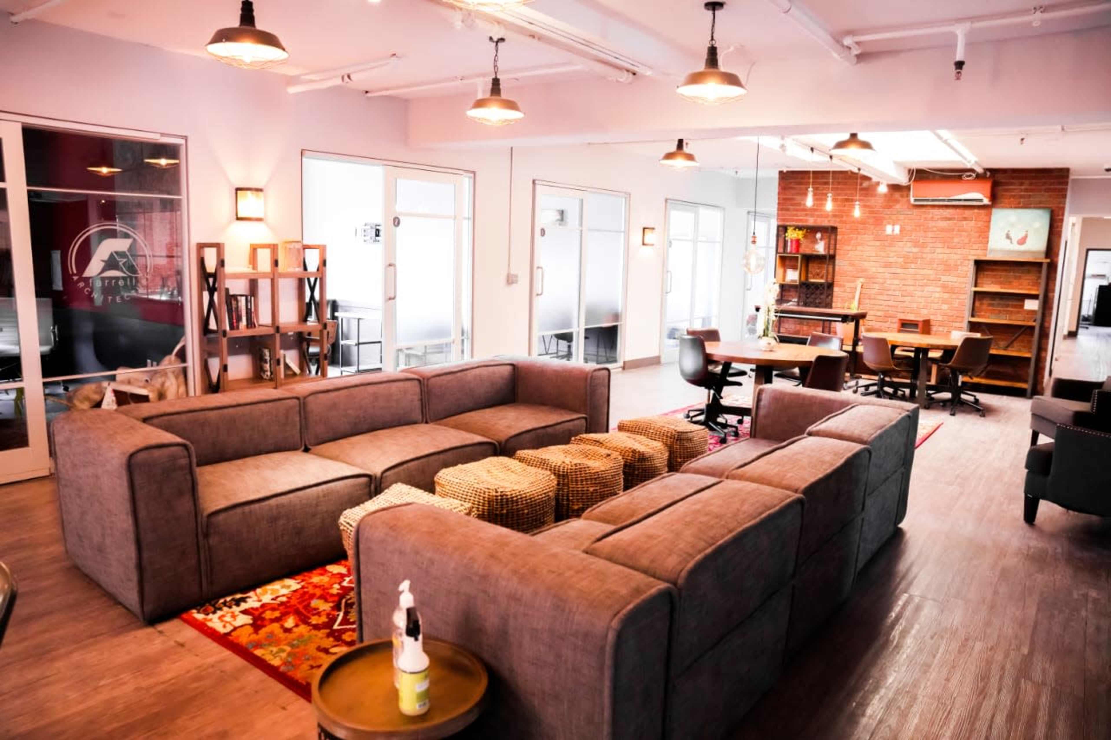 A modern lounge area featuring a large sectional sofa, woven ottomans, and a mix of wooden and metal furniture in a well-lit space.