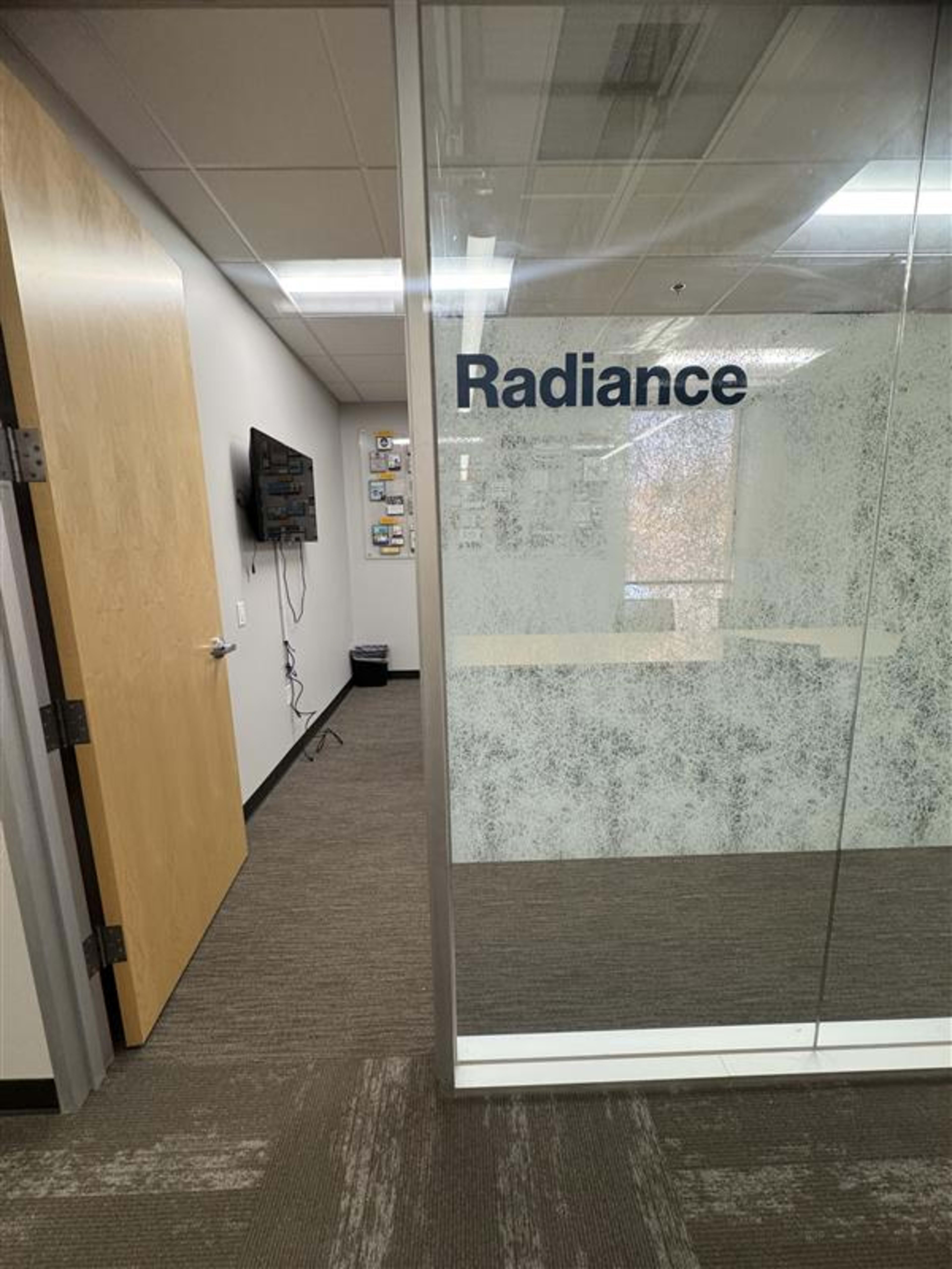 The image shows a glass-walled office with the word "Radiance" displayed prominently, and a door leading into the space.