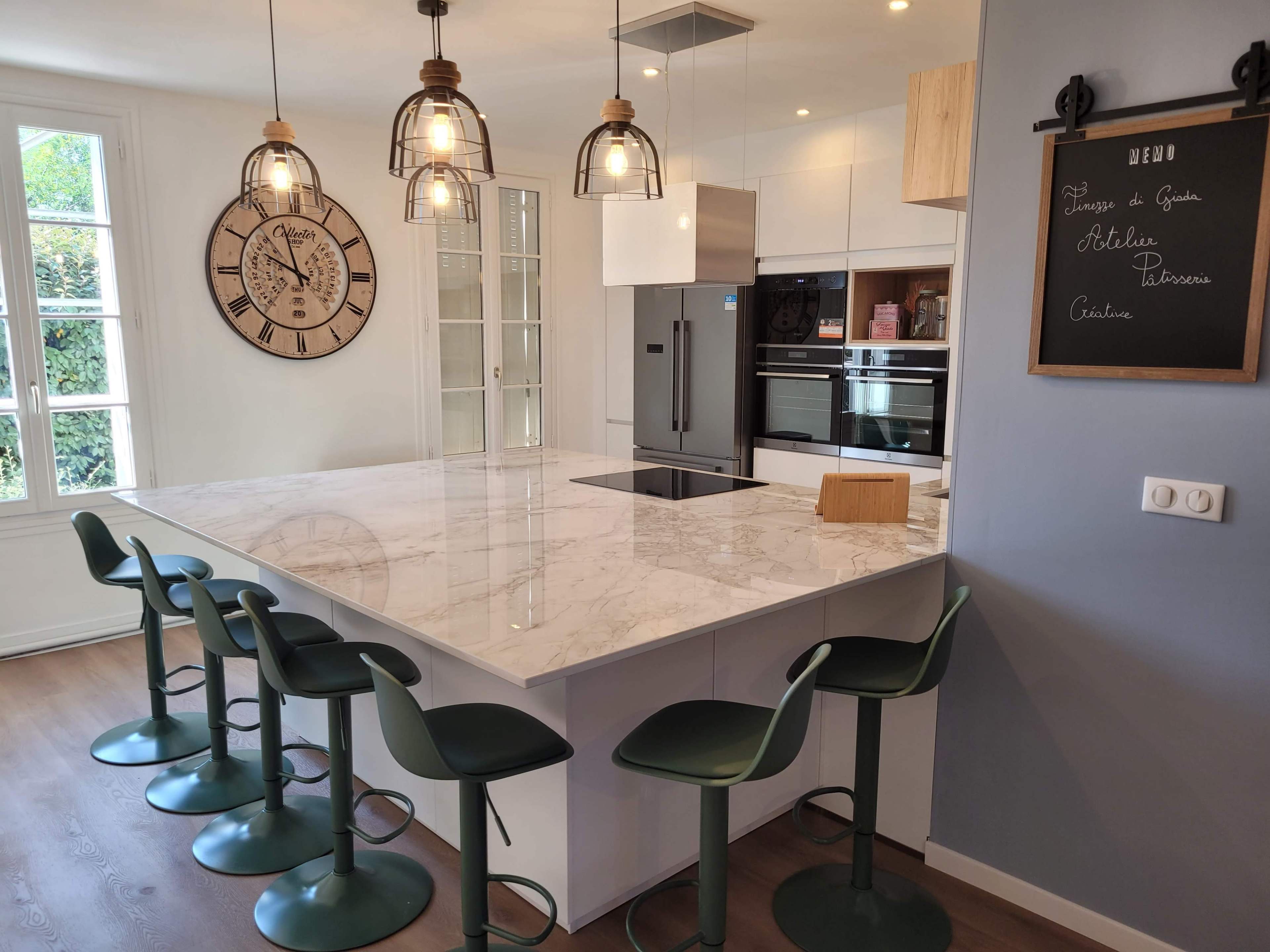 A modern kitchen with a marble island, green bar stools, and a large wall clock.