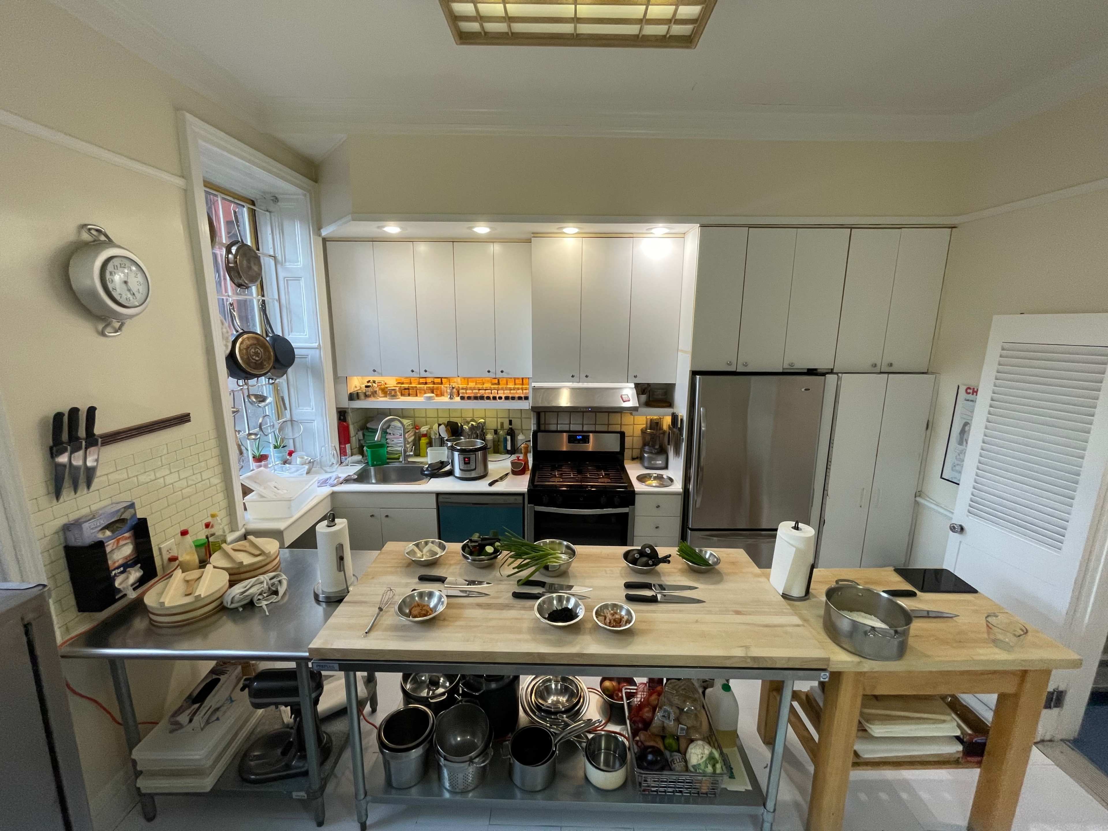 A modern kitchen features a central wooden island surrounded by various cooking appliances, utensils, and ingredients on the counters.