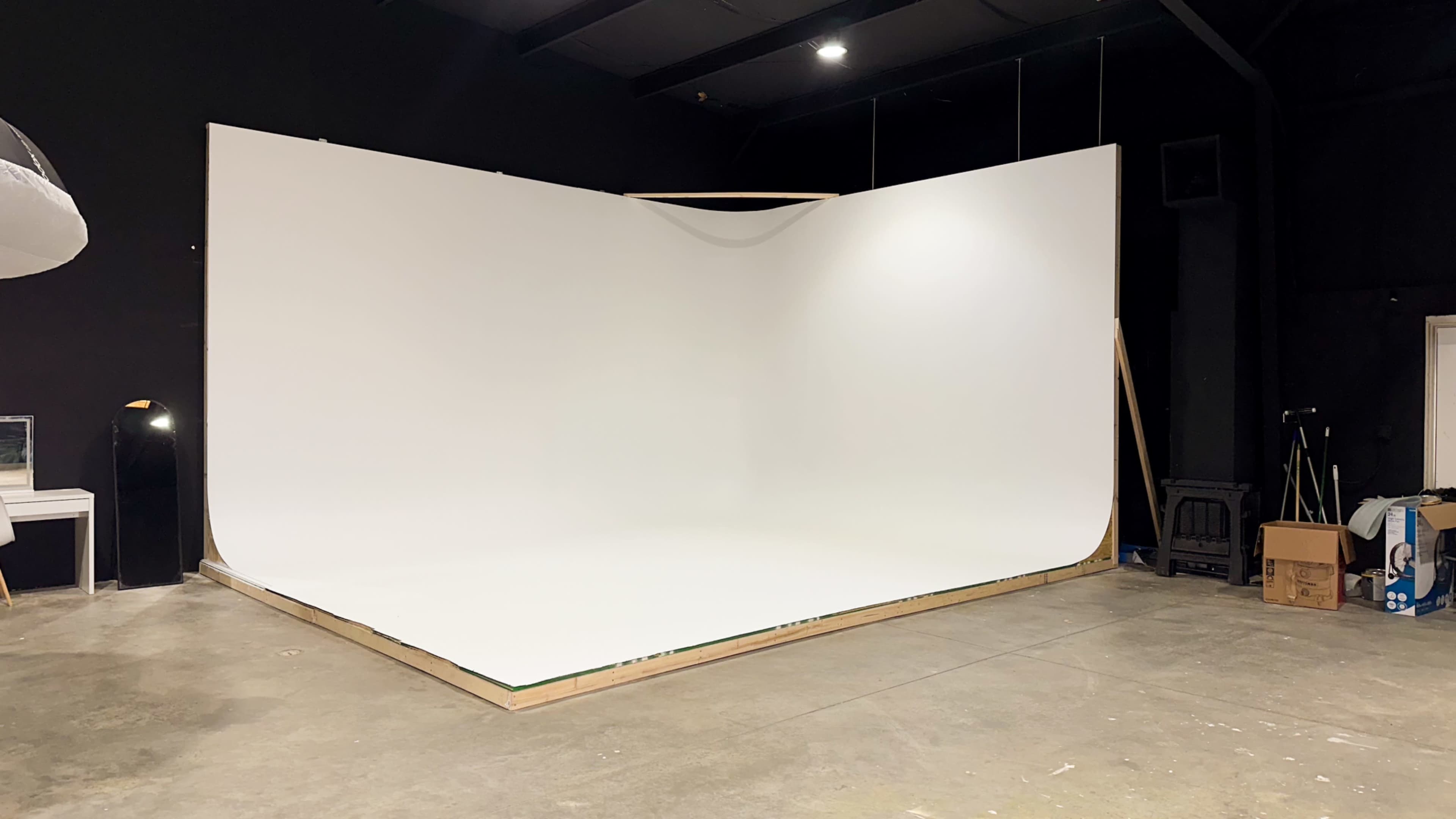 The image shows a spacious photo studio with a seamless white backdrop and a polished concrete floor.