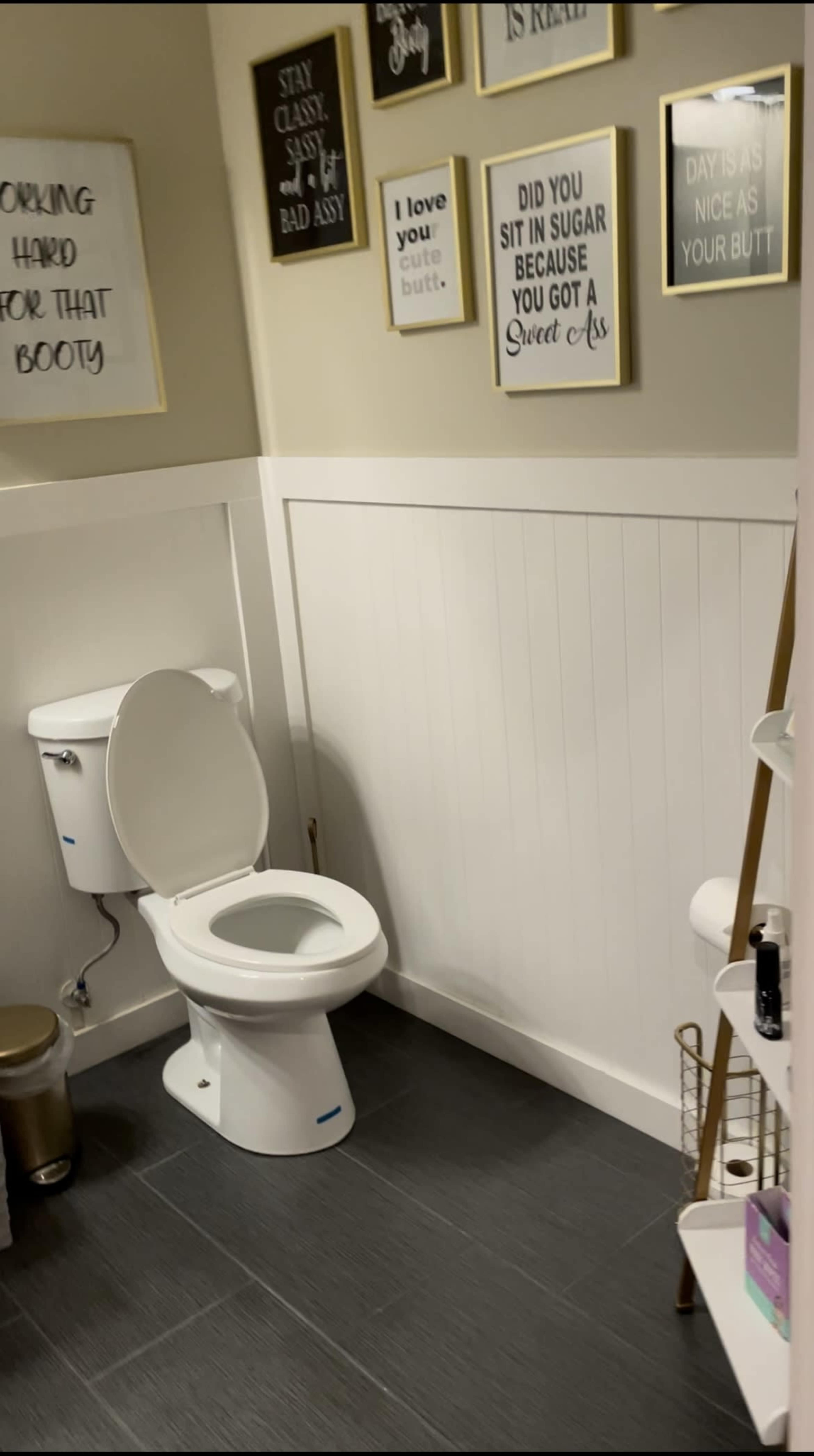 A bathroom with a white toilet, decorative framed quotes on the wall, and storage shelves.