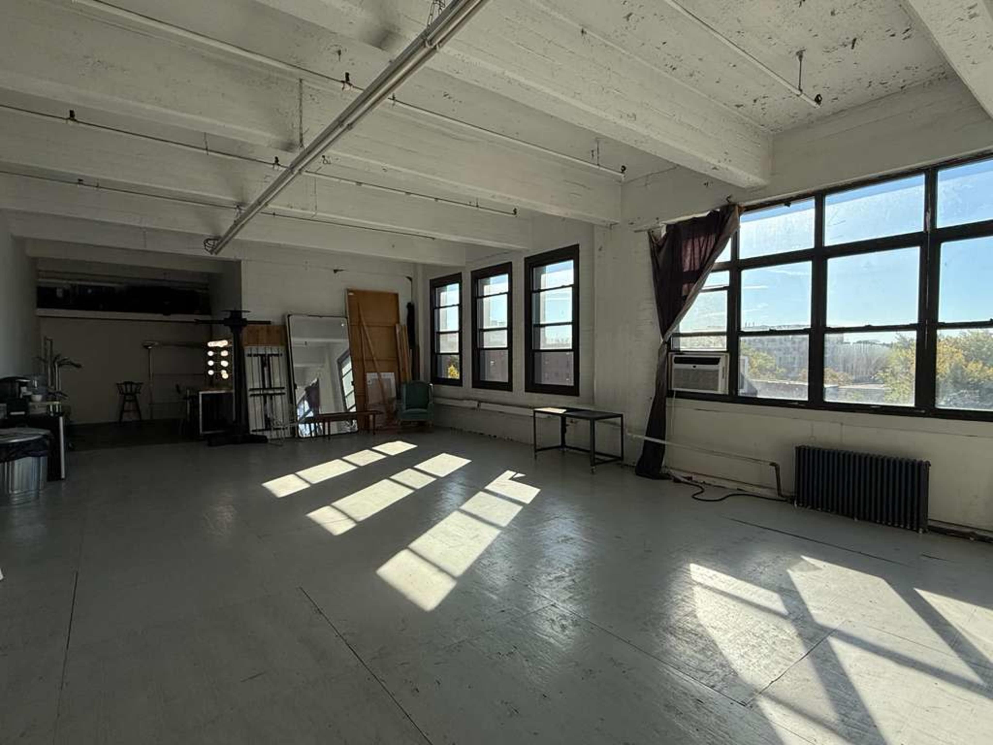 The image shows a spacious, empty room with large windows that allow natural light to cast shadows on the floor.