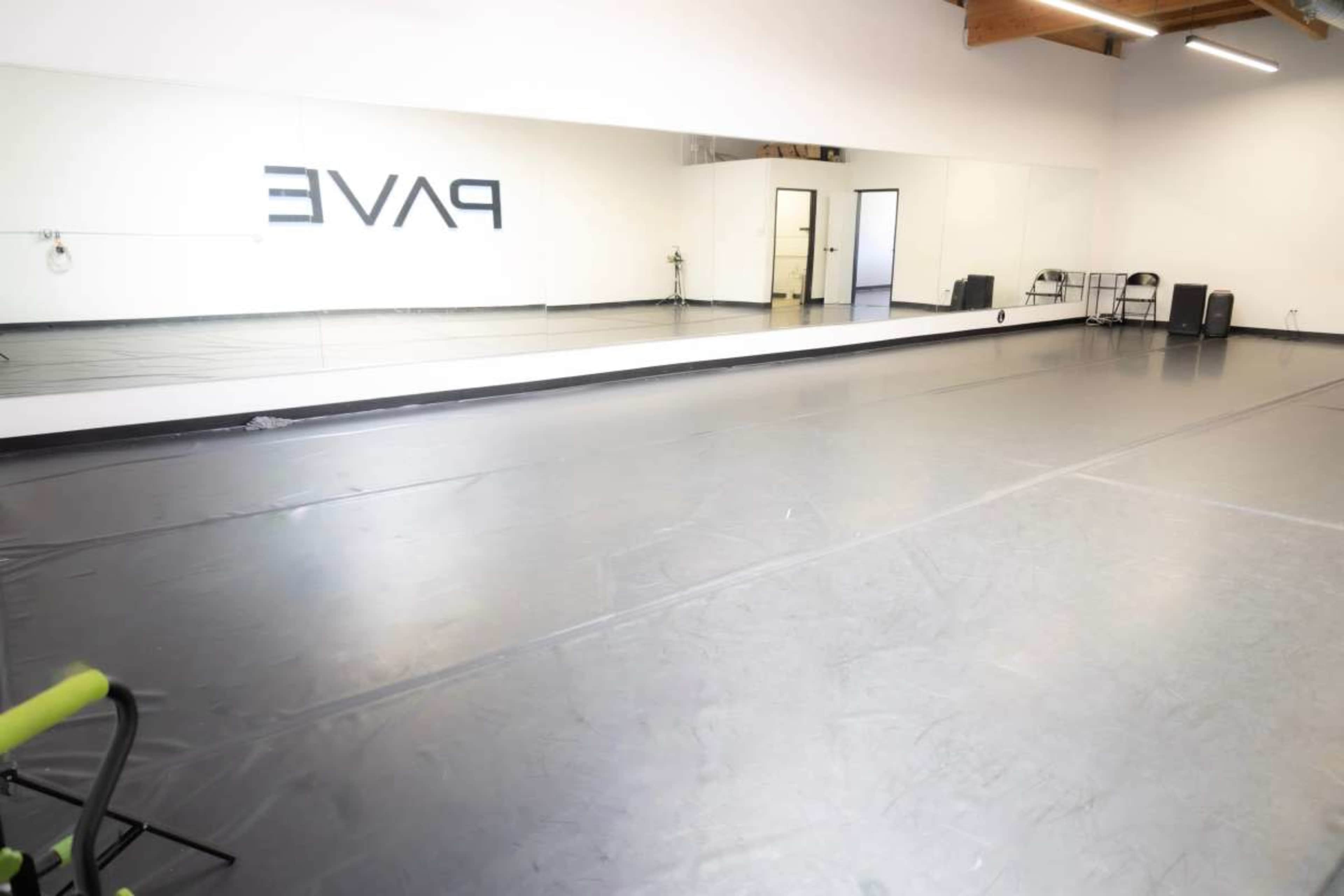 The image shows a spacious dance studio featuring a reflective wall mirror and a smooth, dark flooring surface.