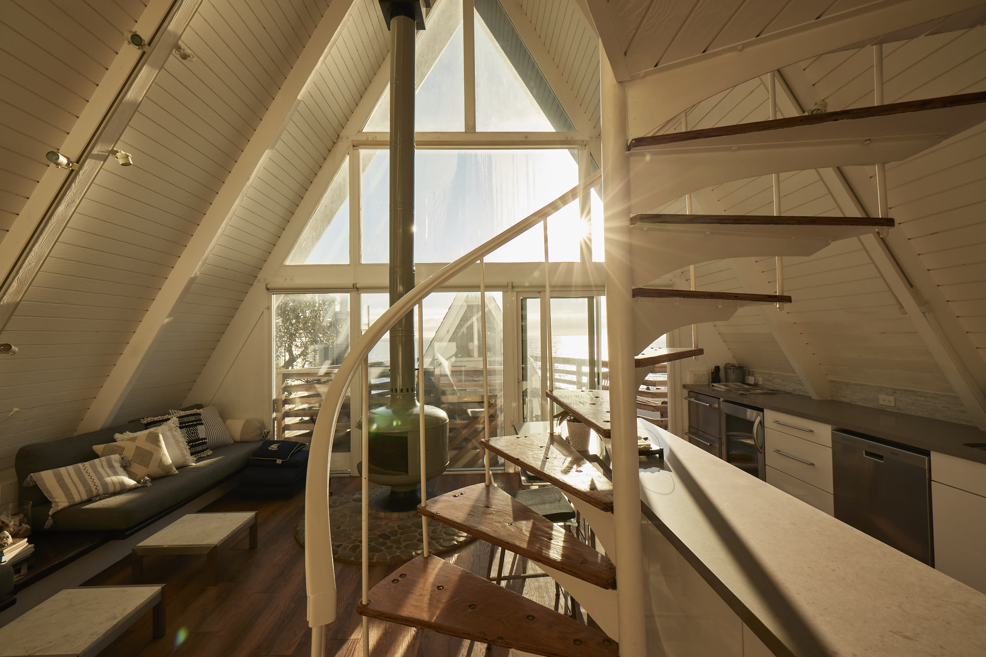 The image depicts a modern A-frame cabin interior featuring a spiral staircase, large windows for natural light, and minimalist furniture.
