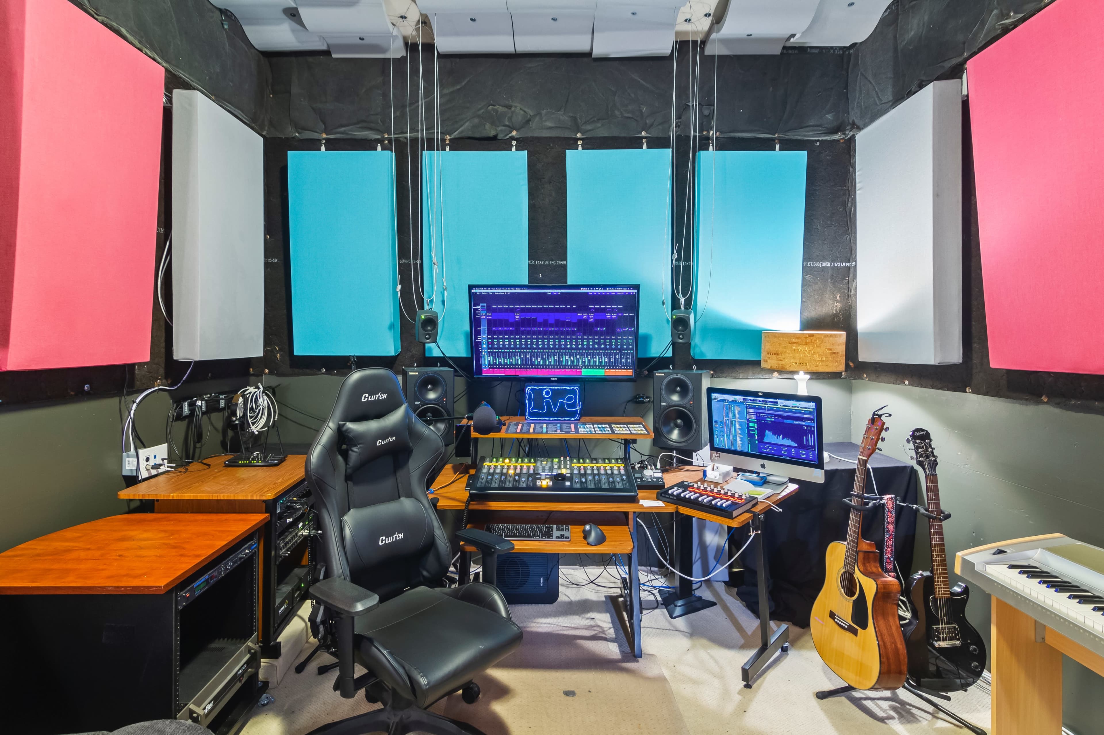 A music studio is equipped with various audio equipment, a computer screen displaying music software, and instruments including a guitar and keyboard.